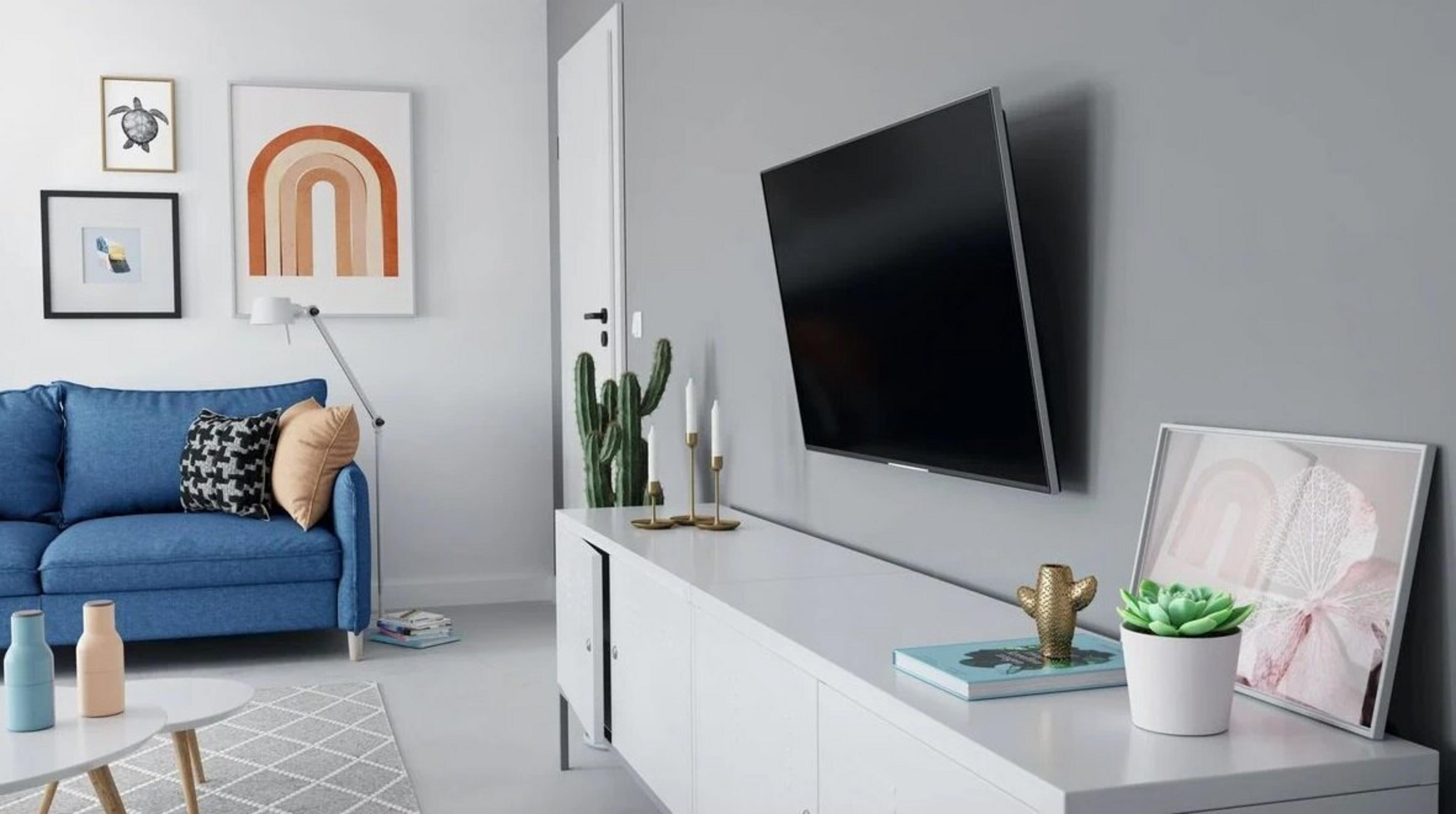 Nowoczesny salon z niebieską sofą, białym meblem i TV na szarej ścianie.