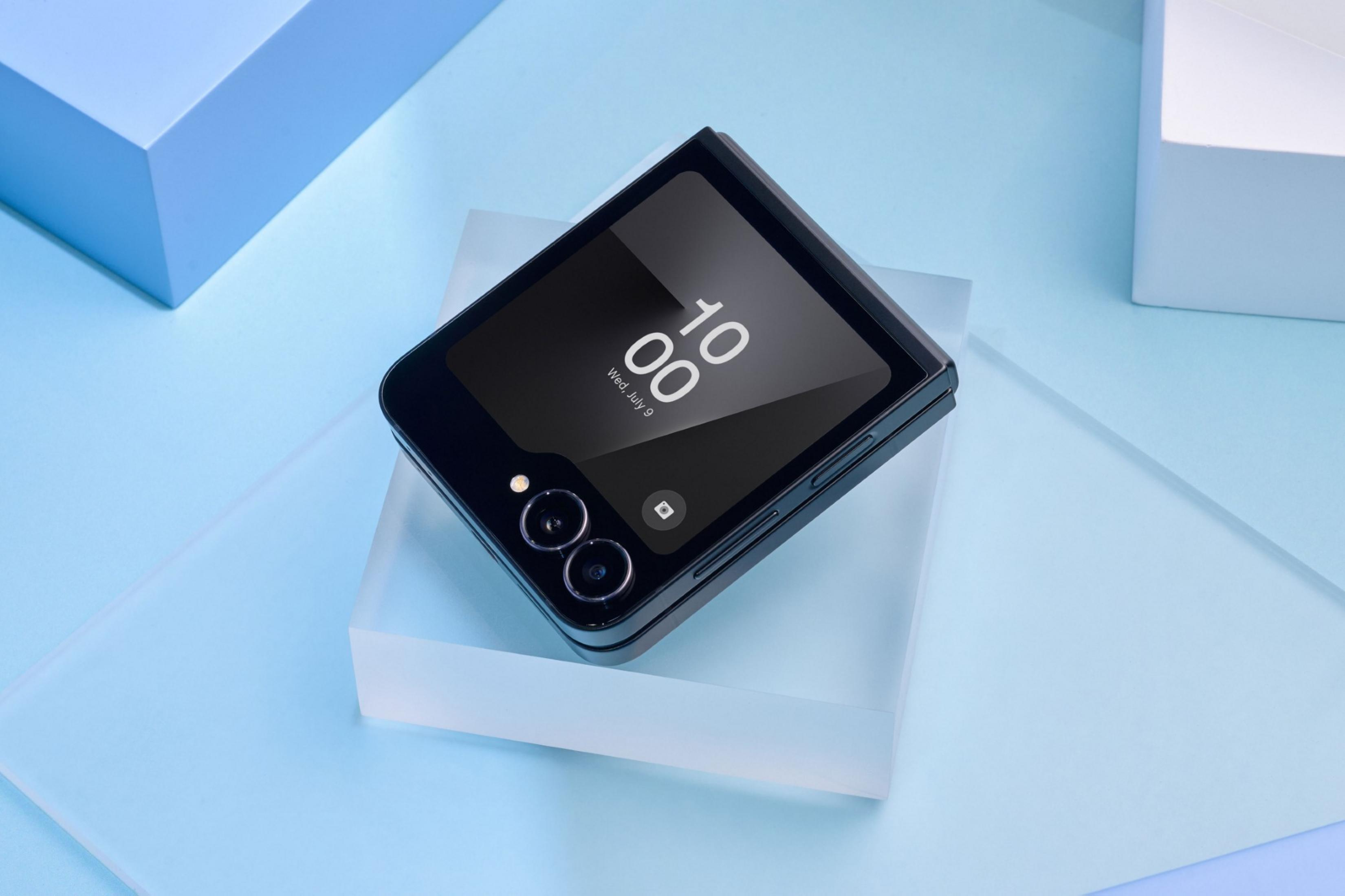 Zamknięty czarny telefon typu flip na przezroczystym bloku, obok niebieskie i białe bloki.