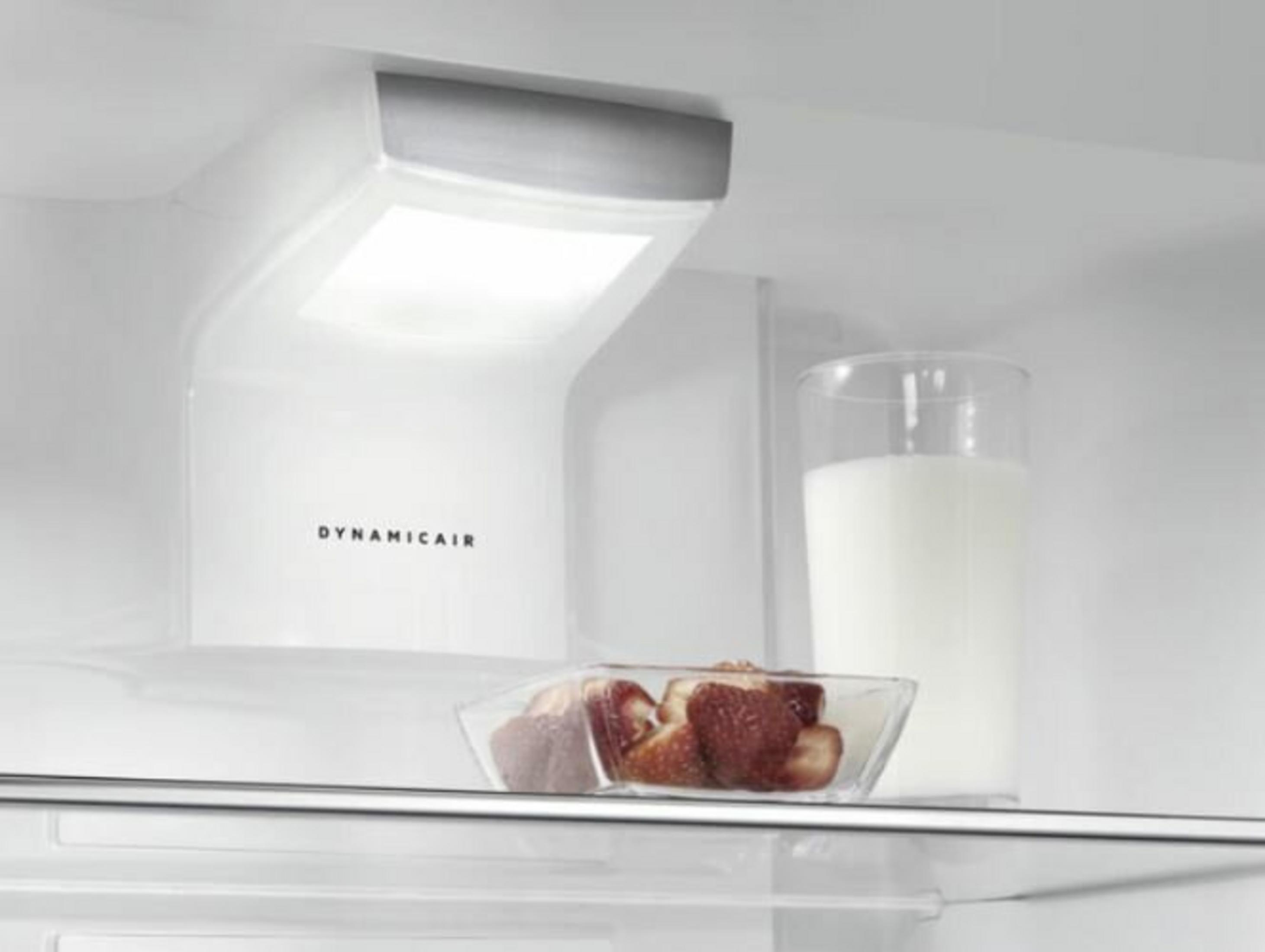 Un vaso de leche y fresas en un bol dentro de un refrigerador.