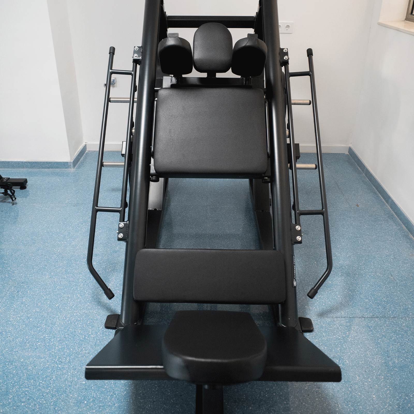 Una máquina de gimnasio negra con acolchado y marco de metal en suelo azul.