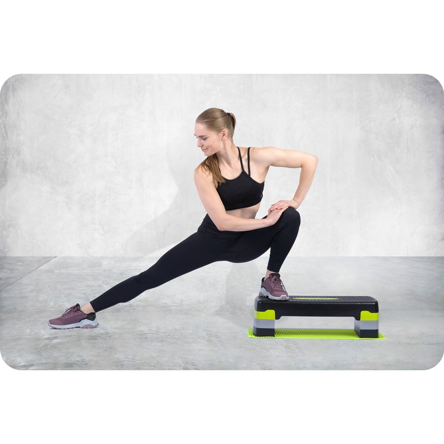 Una mujer se estira en una plataforma de step aeróbico en un gimnasio.