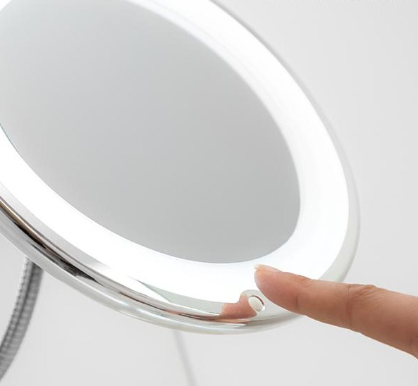 Una mano preme il pulsante di accensione di uno specchio per il trucco illuminato.