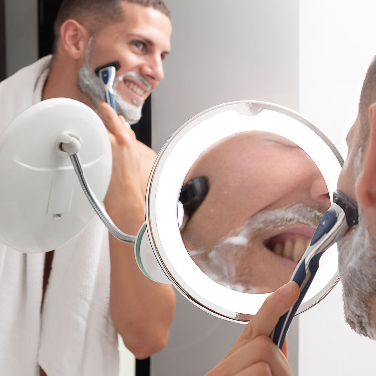 Uomo con schiuma da barba sul viso si rade con un rasoio davanti a uno specchio illuminato.