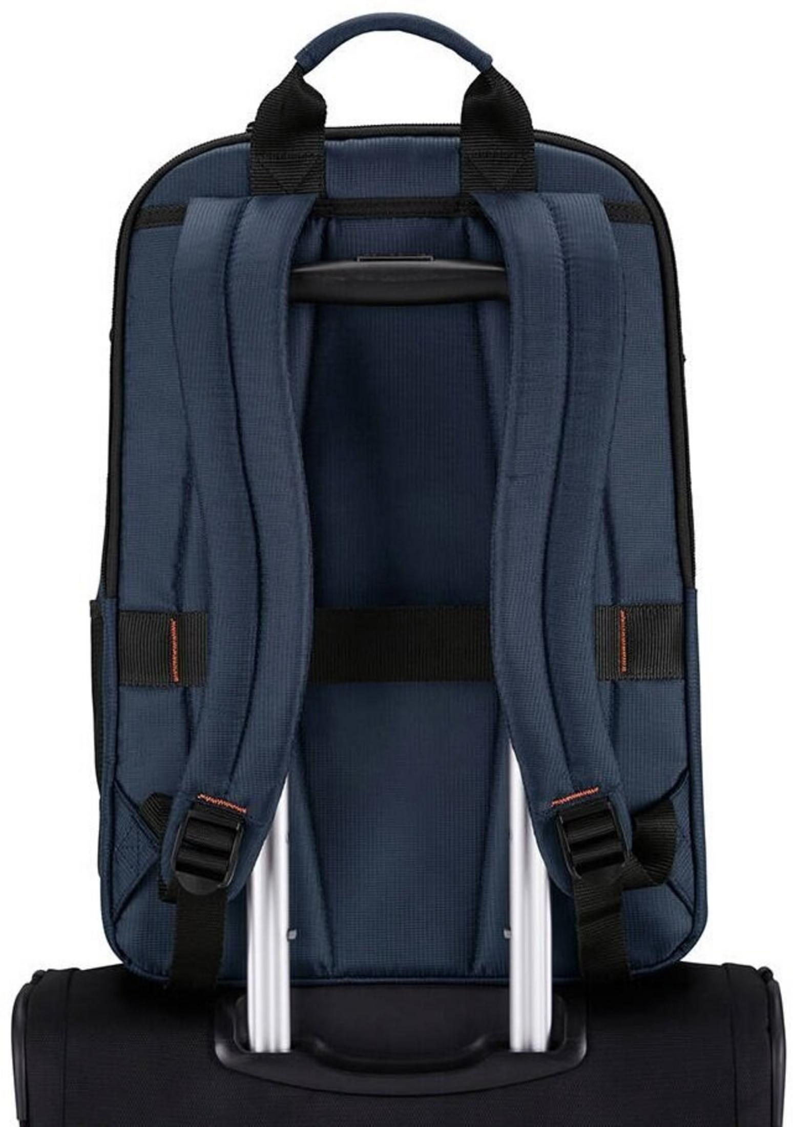 Una mochila azul marino con correas negras está sujeta al asa de una maleta negra.