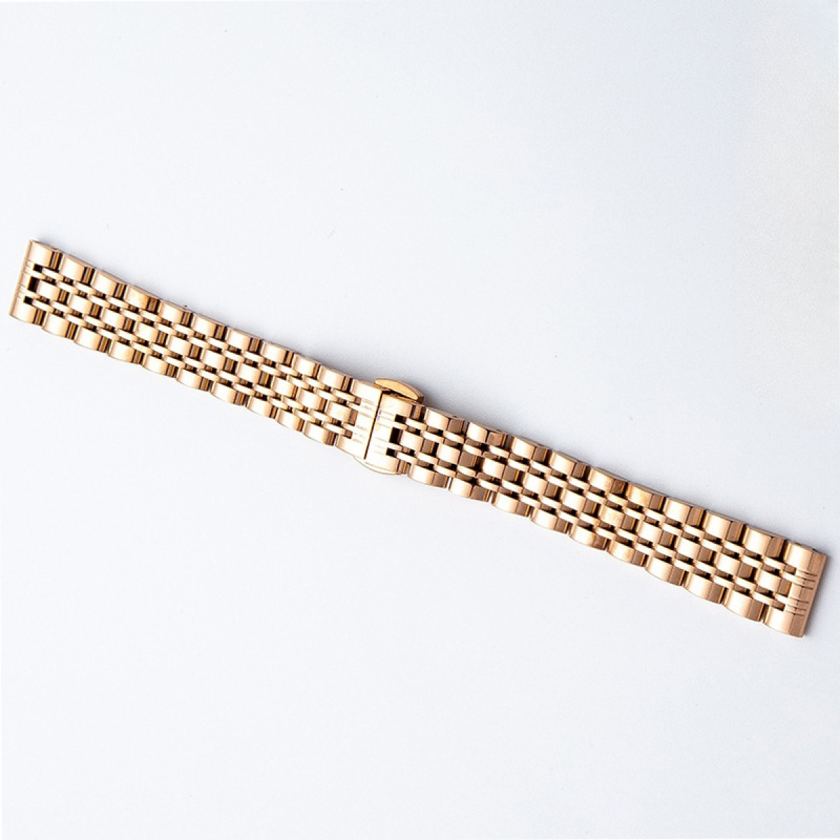 Ein roségoldenes Metalluhrenarmband mit Faltschließe liegt auf weißem Grund.