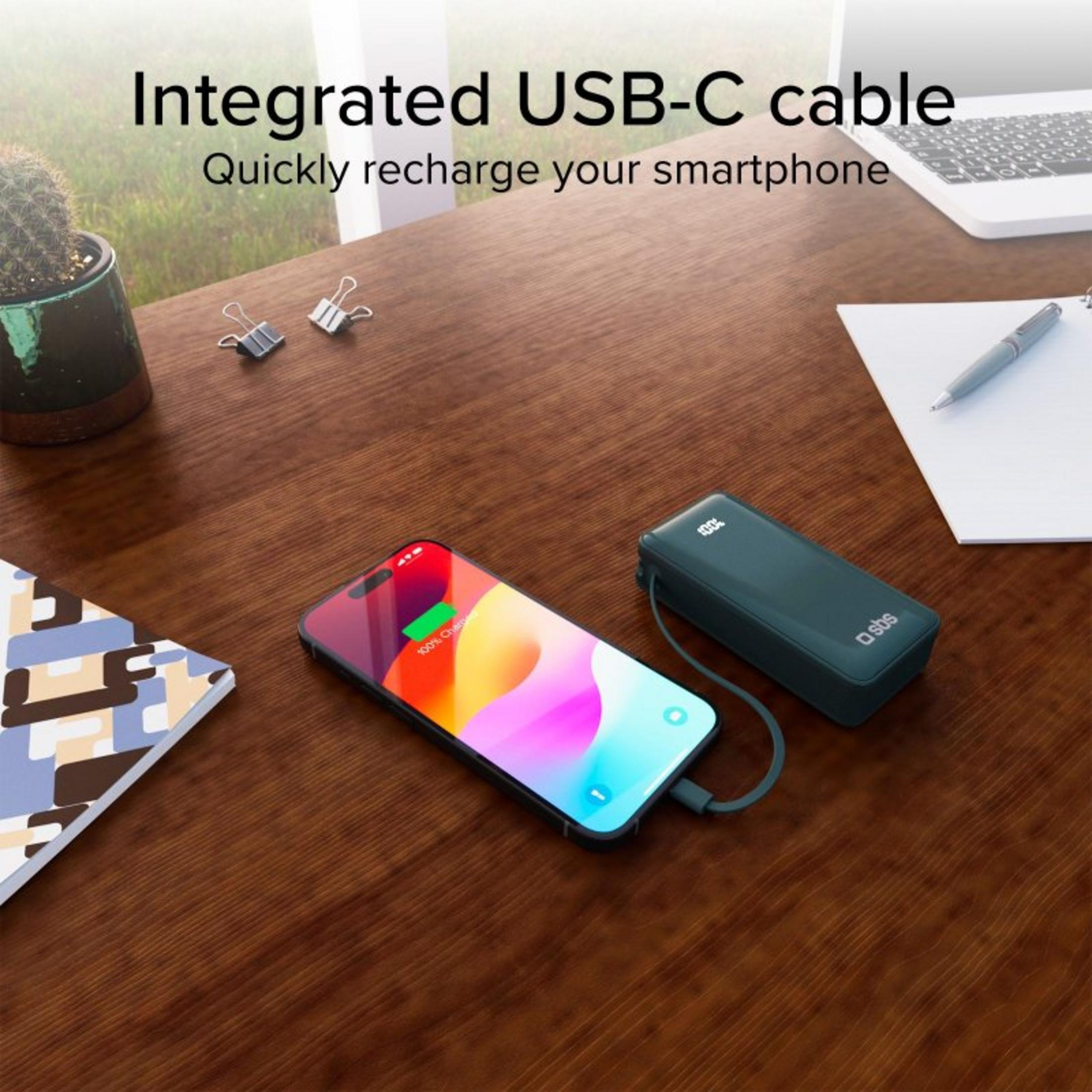 Power bank verde scuro carica uno smartphone su una scrivania di legno. Cavo USB-C integrato.
