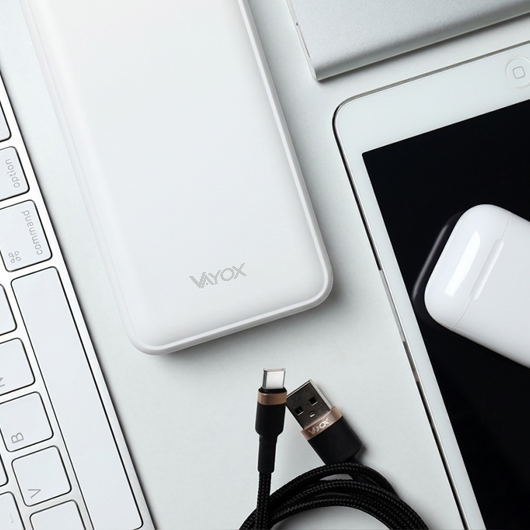 Biały power bank, klawiatura, tablet i kabel do ładowania na białej powierzchni.