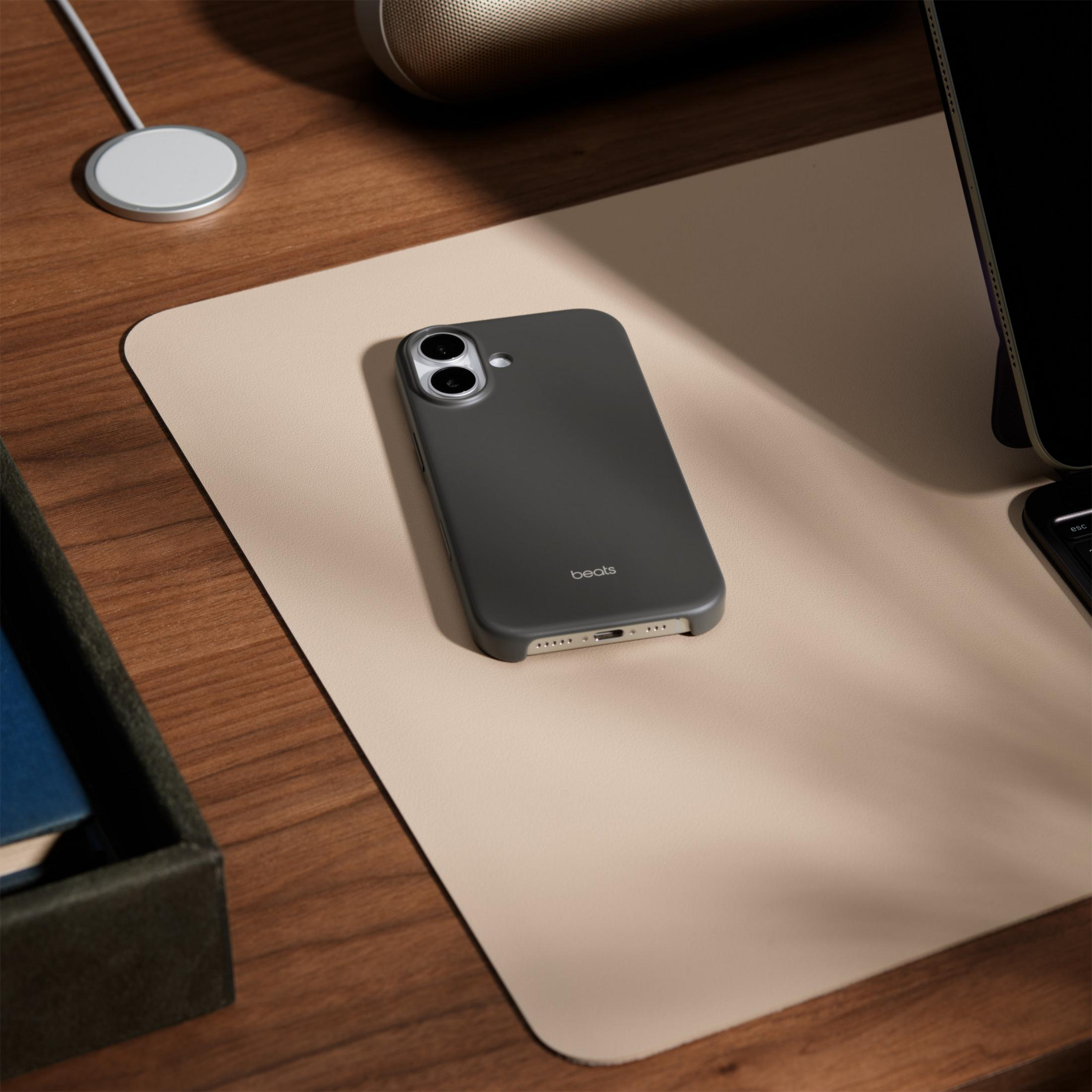 Ein dunkelgraues Handy mit 'beats'-Logo liegt auf einer beige Matte auf einem Holztisch.