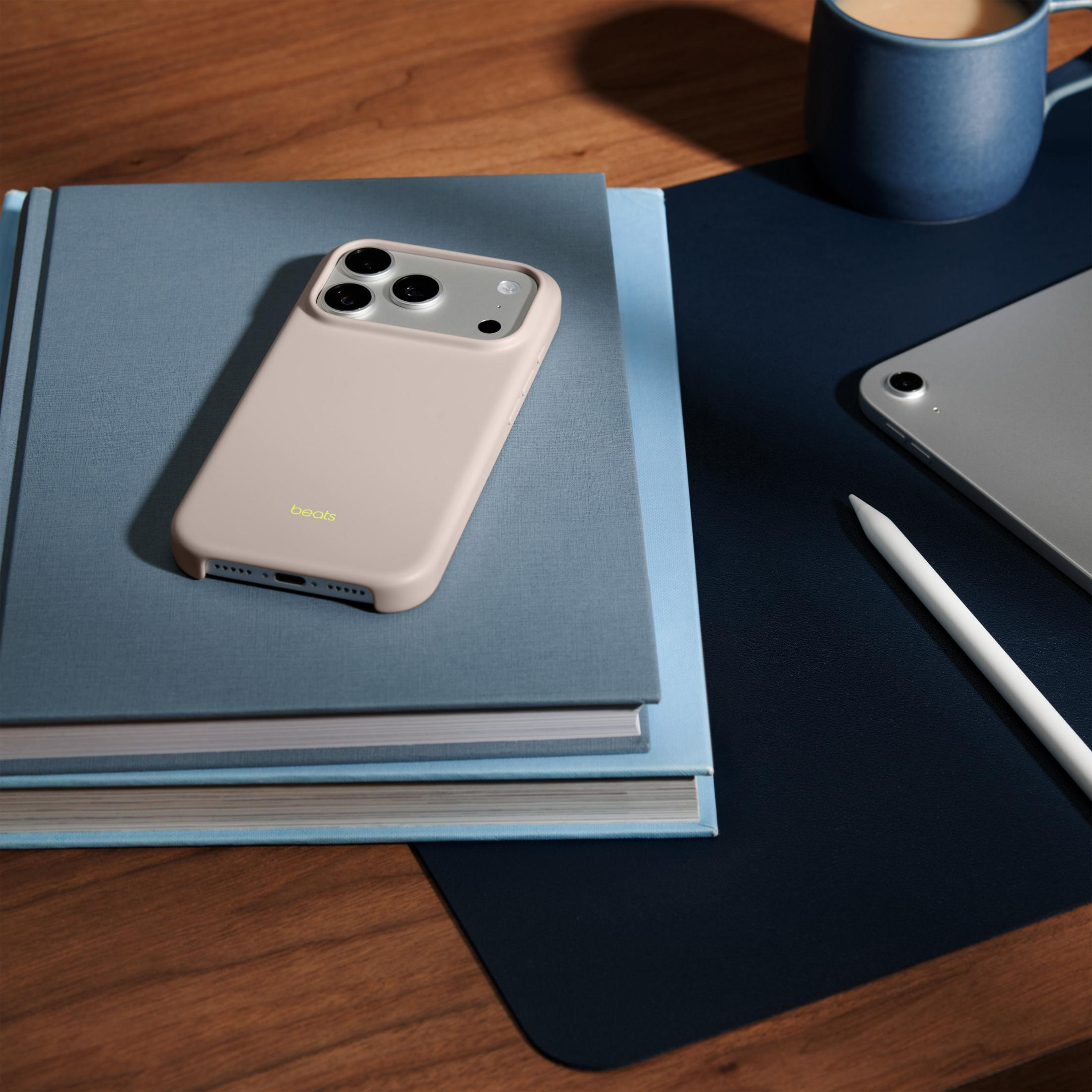 Jasnoróżowe etui na telefon leży na dwóch niebieskich książkach. Obok jest tablet, długopis i kubek.