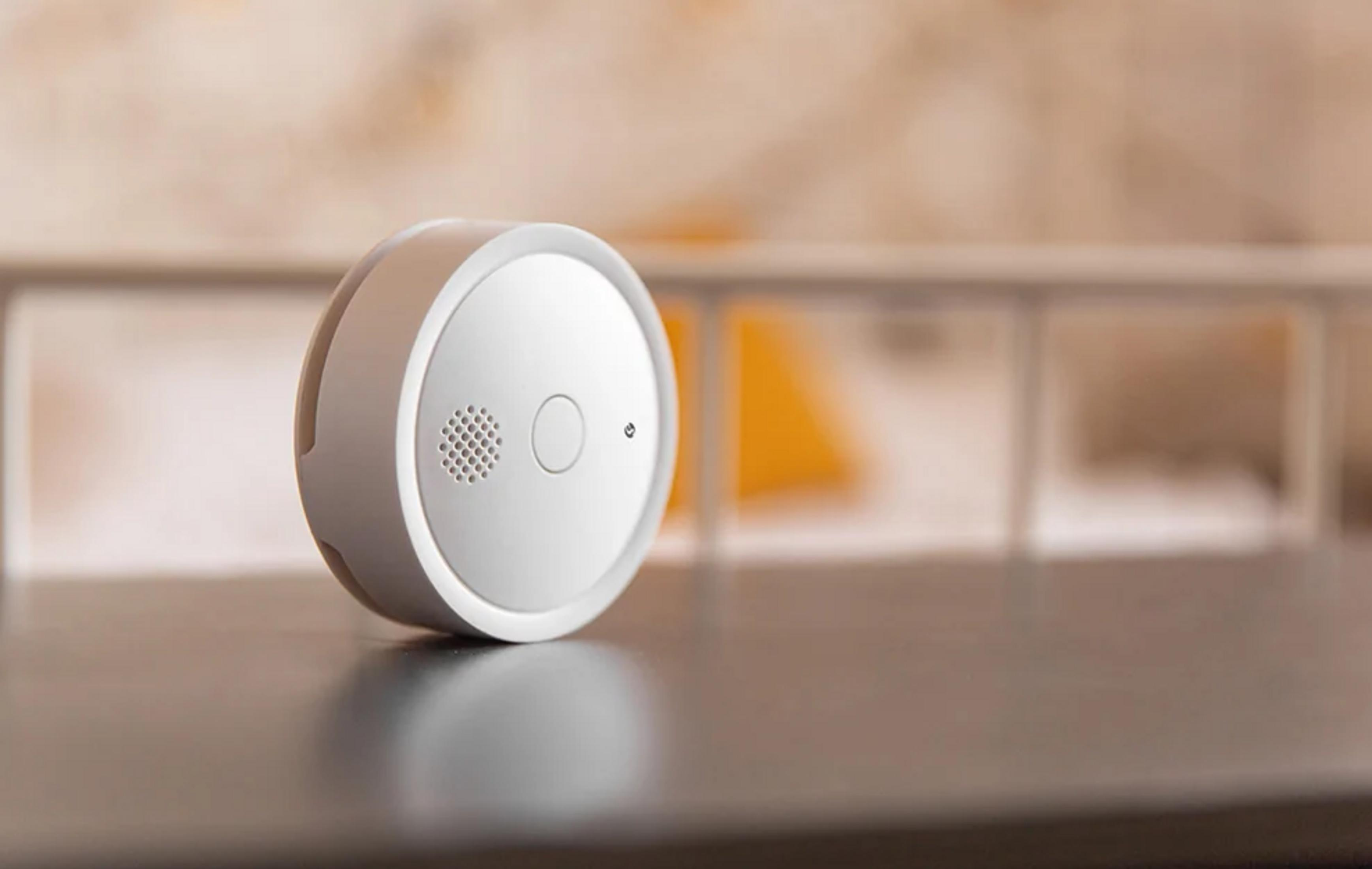 Biały czujnik dymu na ciemnej powierzchni, rozmyte tło.