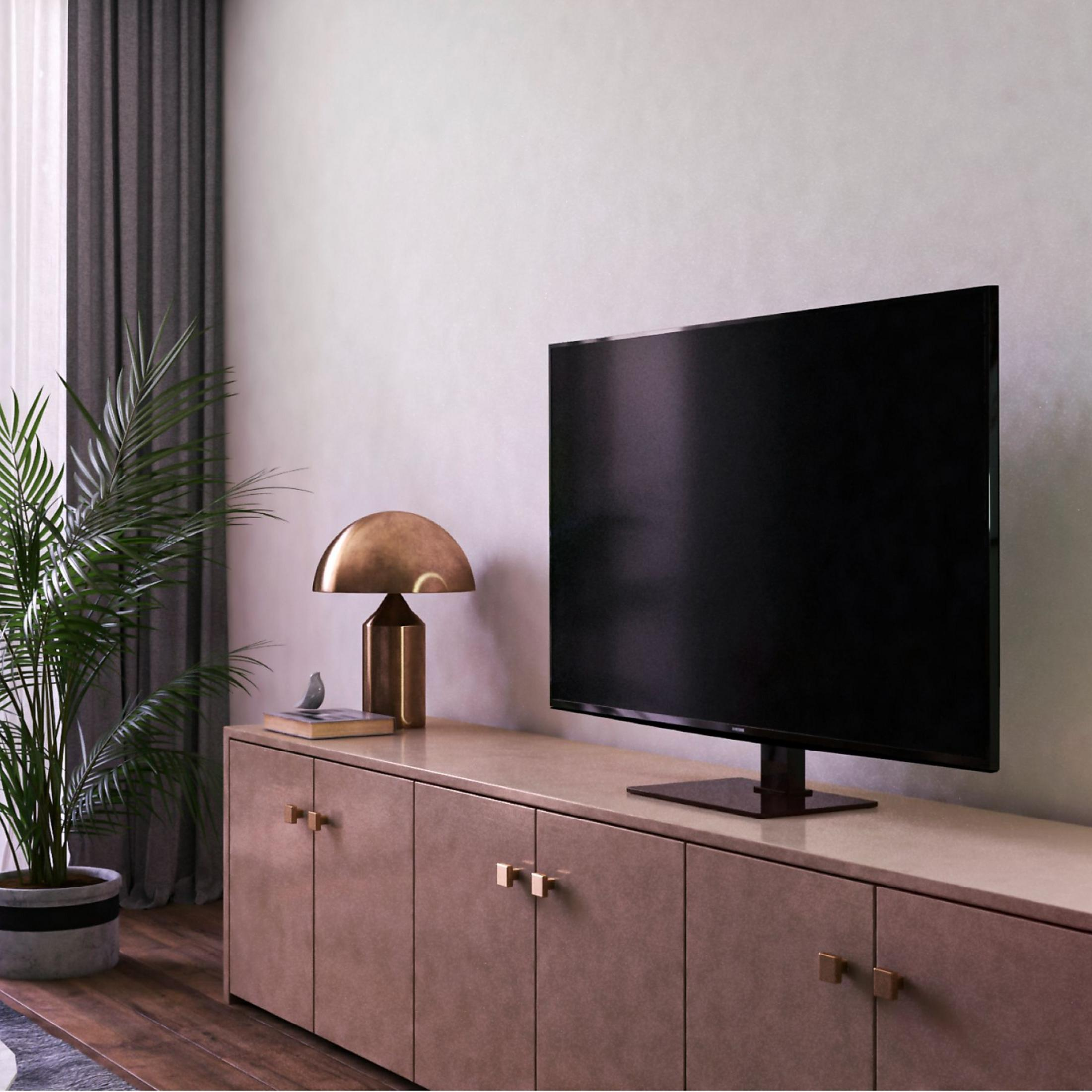 Una sala de estar moderna con TV en consola, lámpara y planta.