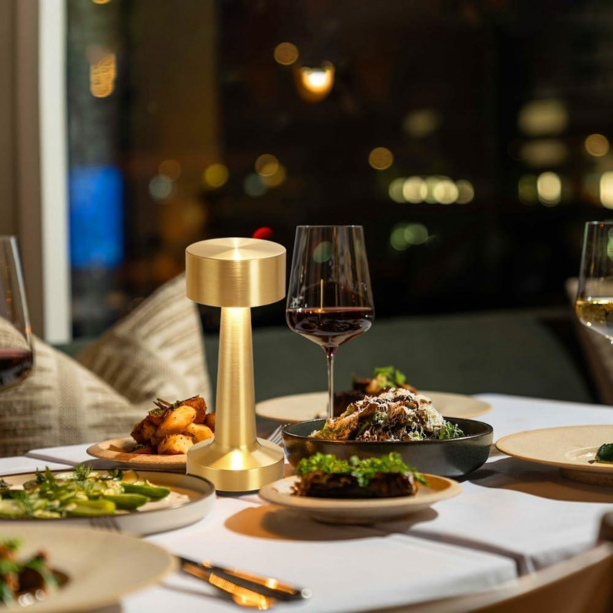 Eine goldene Lampe beleuchtet einen für das Abendessen gedeckten Tisch mit Weingläsern und Essen.