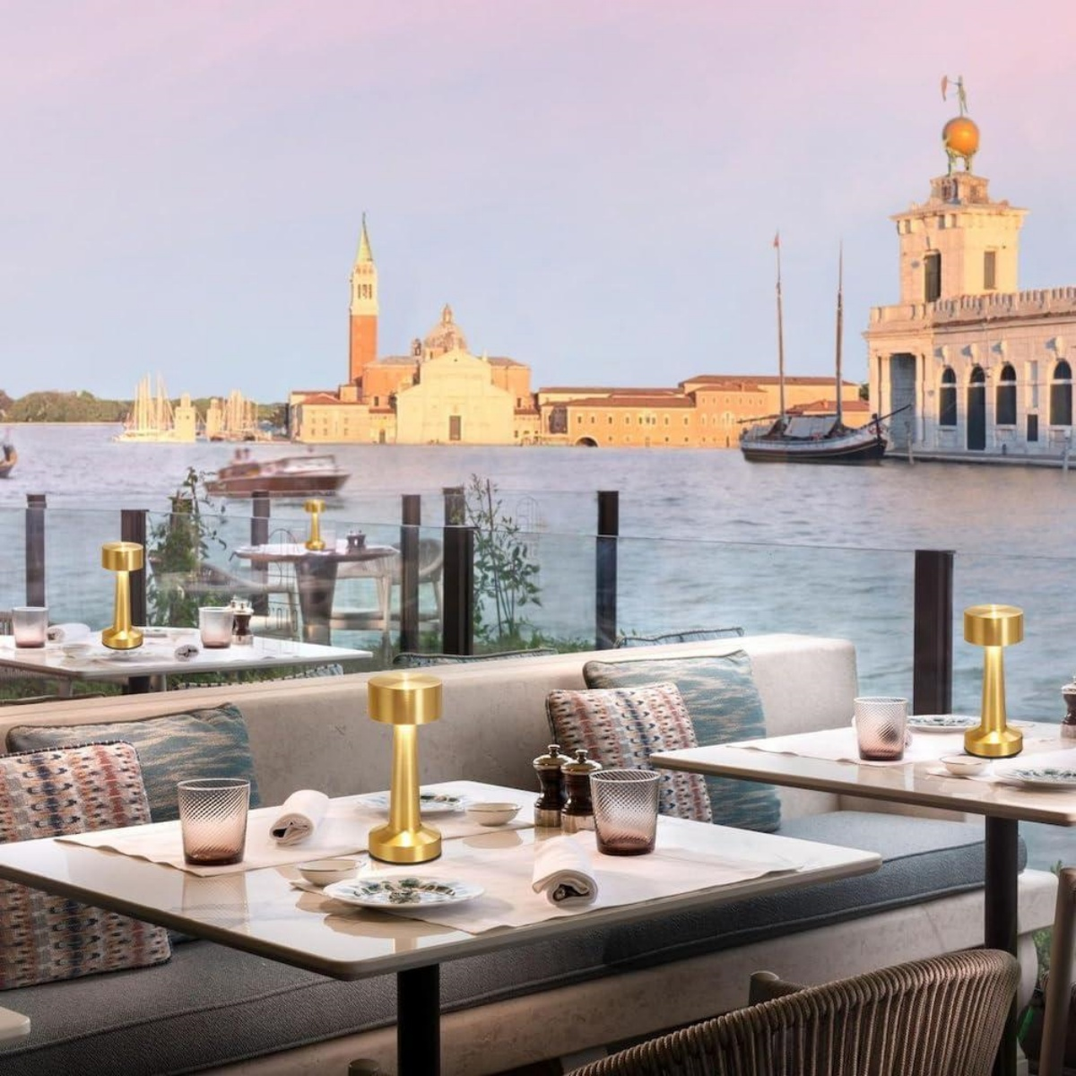 Außenterrasse mit Blick auf Venedig, Tische mit Lampen, Gläsern und Geschirr.