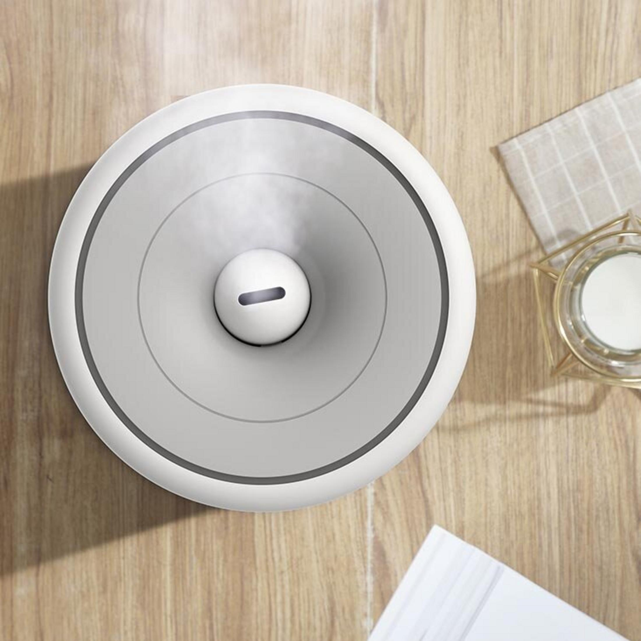 Biały nawilżacz emitujący mgiełkę na drewnianej powierzchni obok świecy.