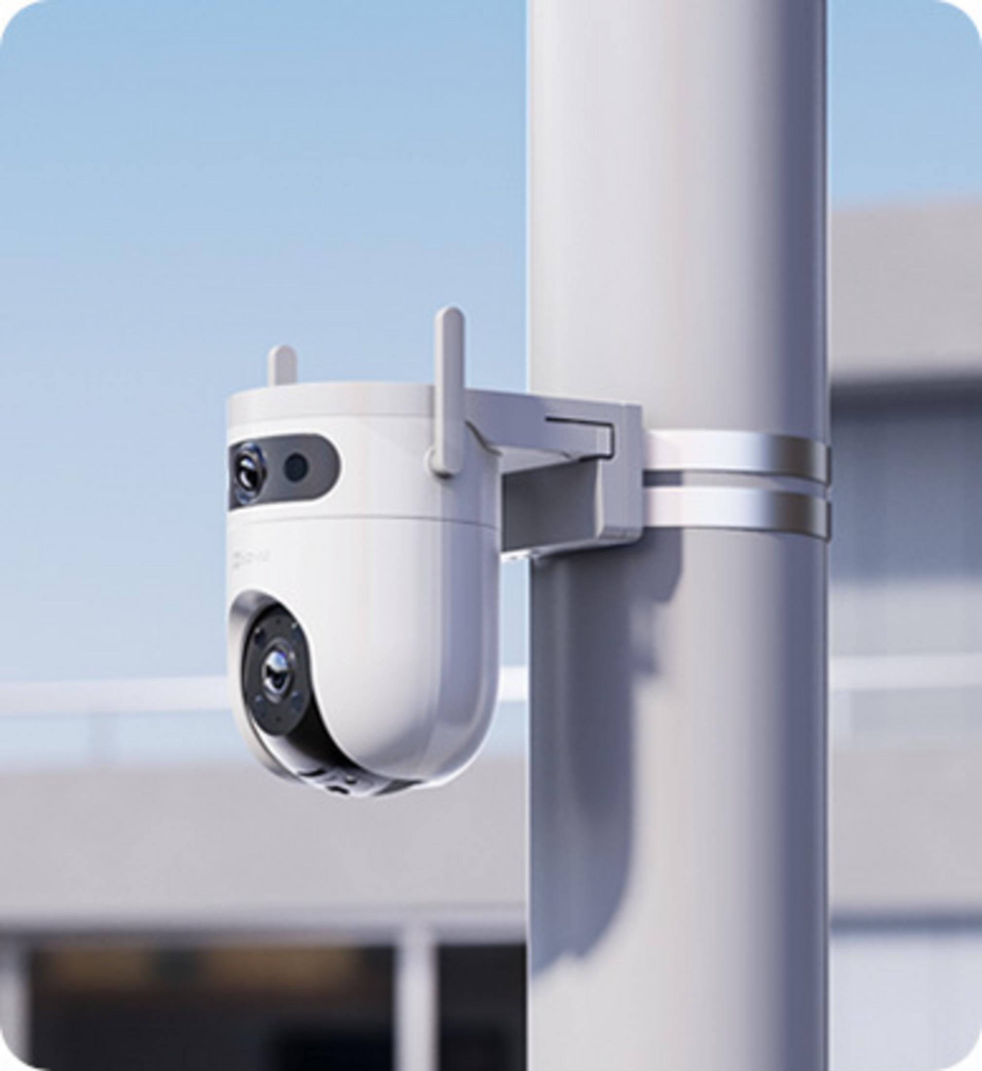 Biała kamera monitoringu zamontowana na szarym słupie. Jasne niebo.