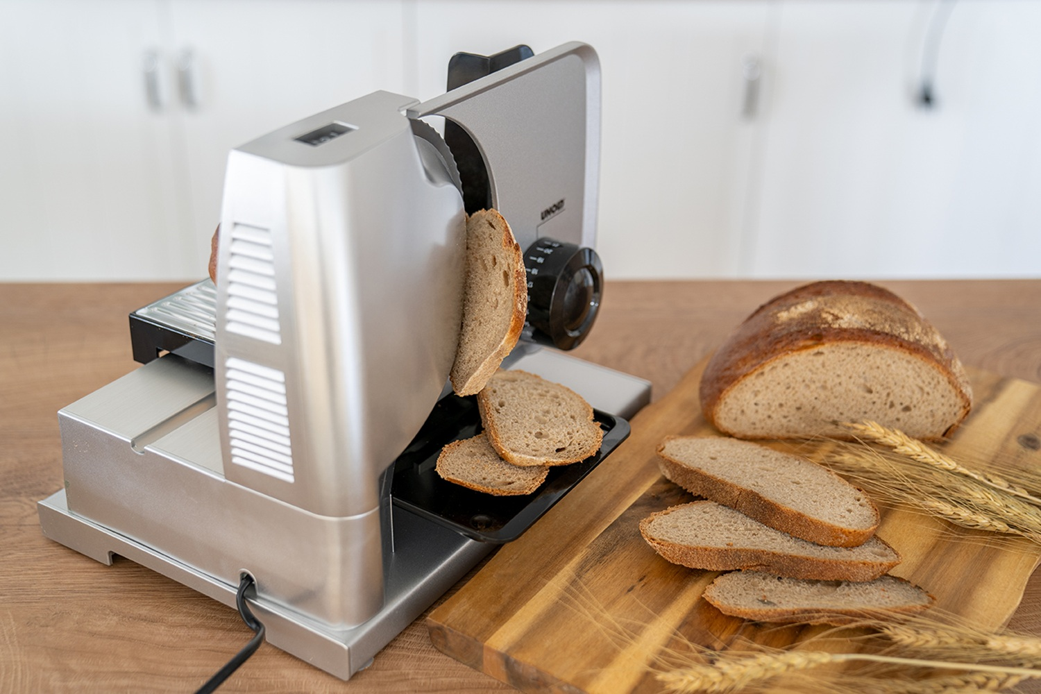 Ein Brotschneider schneidet Brot in Scheiben, daneben liegen Brotscheiben und ein Brot.