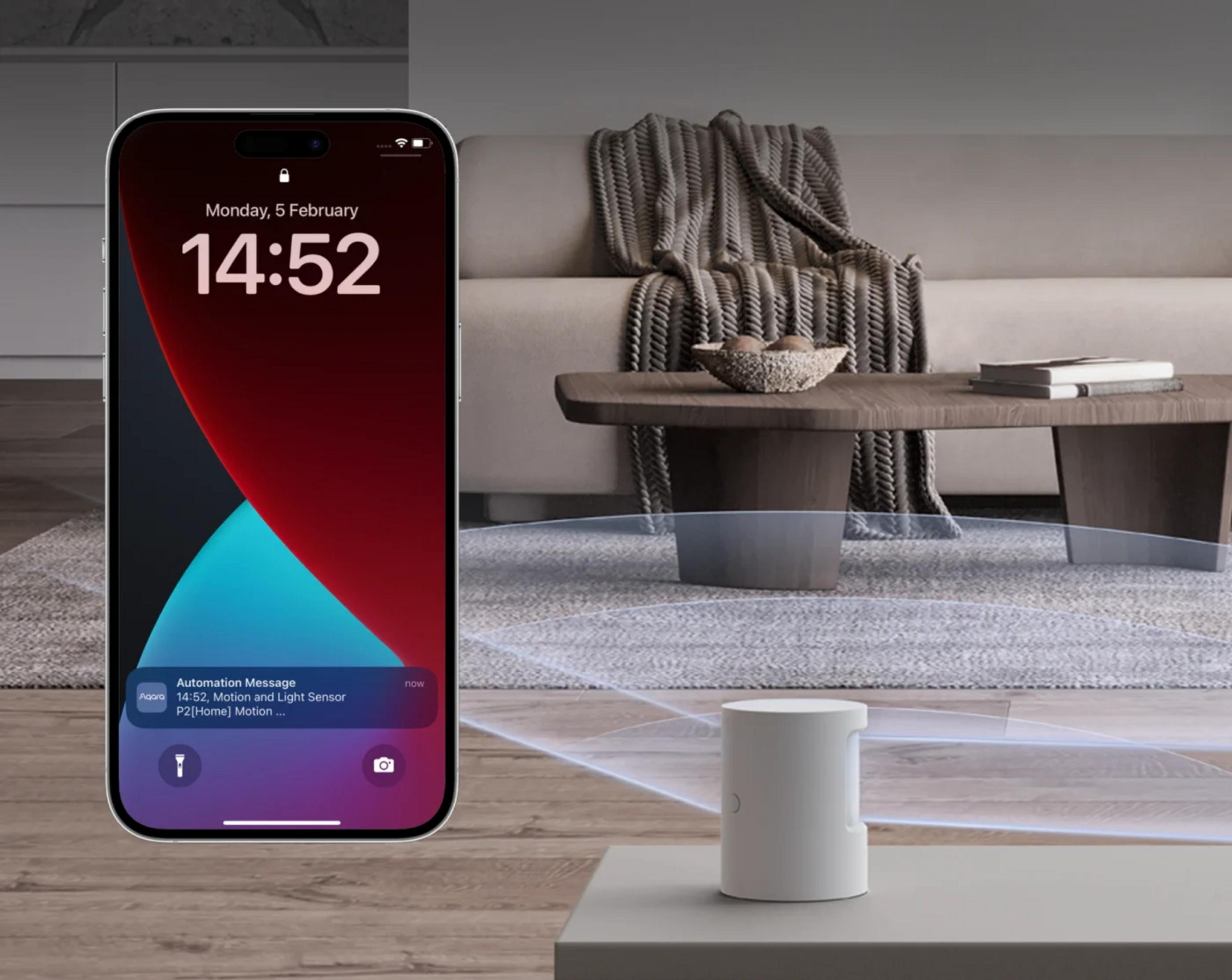 L'iPhone mostra le 14:52, con notifica. Un sensore bianco in un salotto.