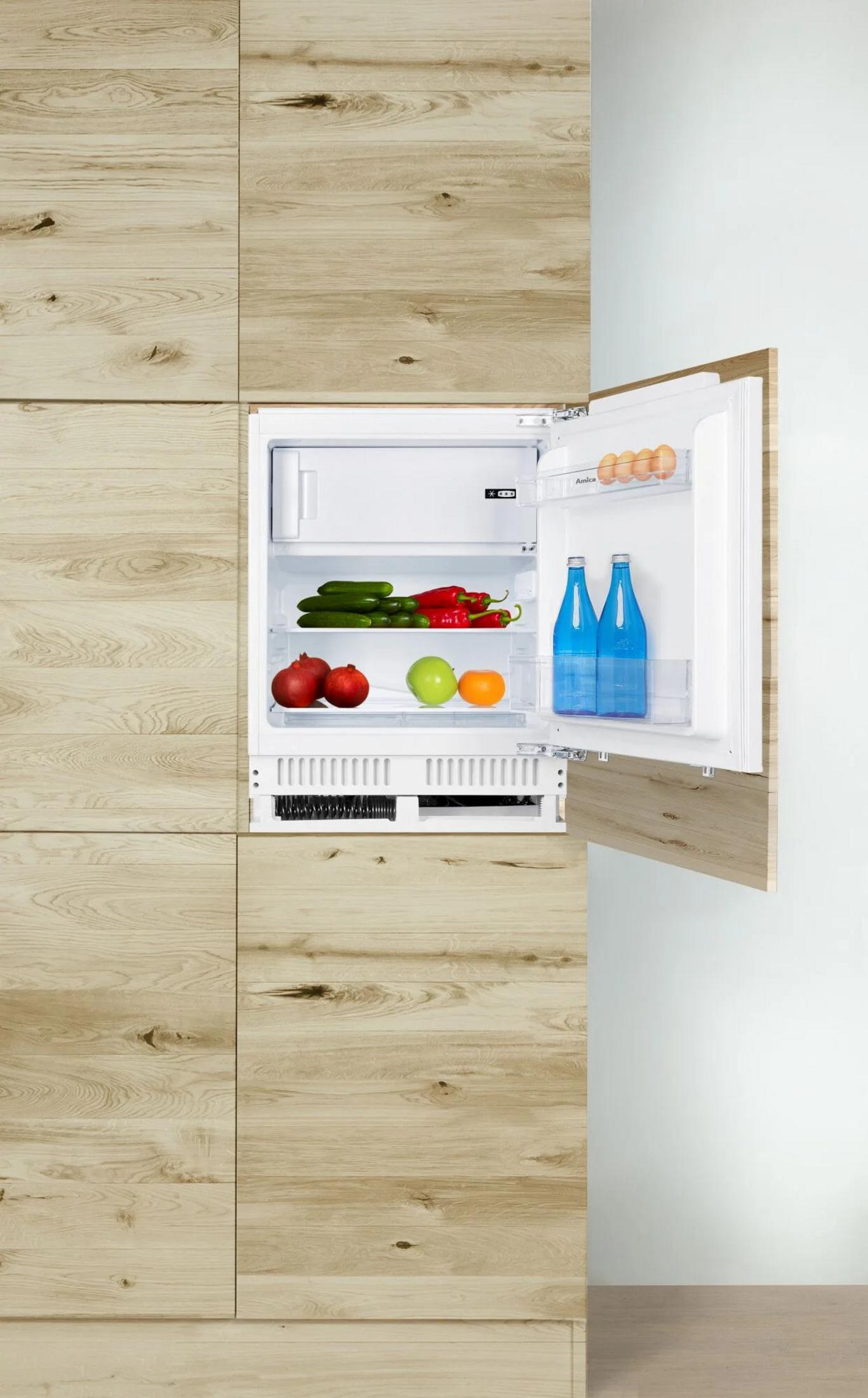 Ein offener Kühlschrank mit Lebensmitteln wie Eiern, Gurken, Paprika, Granatäpfeln, einem Apfel und zwei Wasserflaschen.
