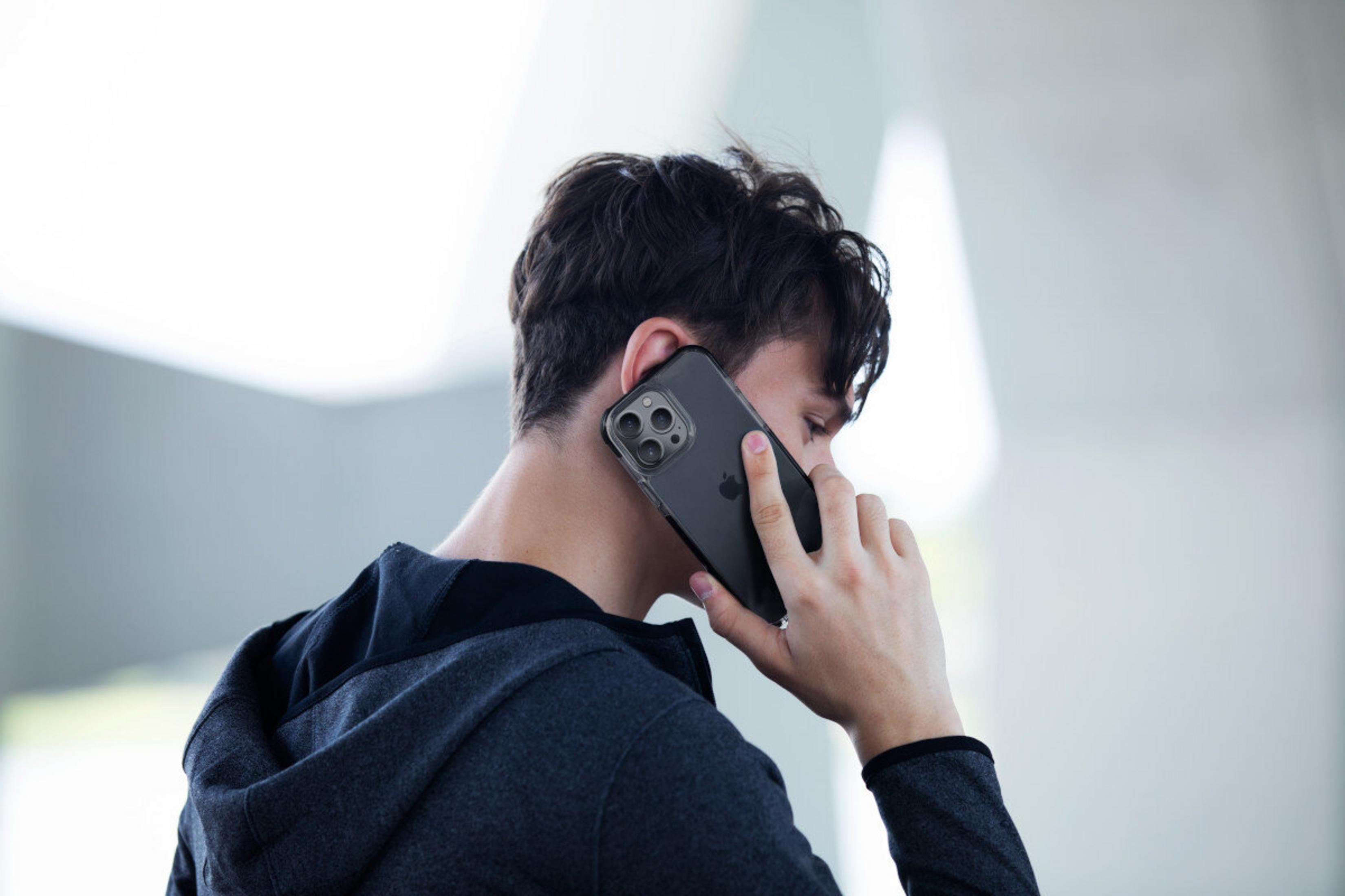 Koyu renk kapüşonlu bir genç, arkadan görünümüyle koyu renkli bir akıllı telefonla konuşuyor.