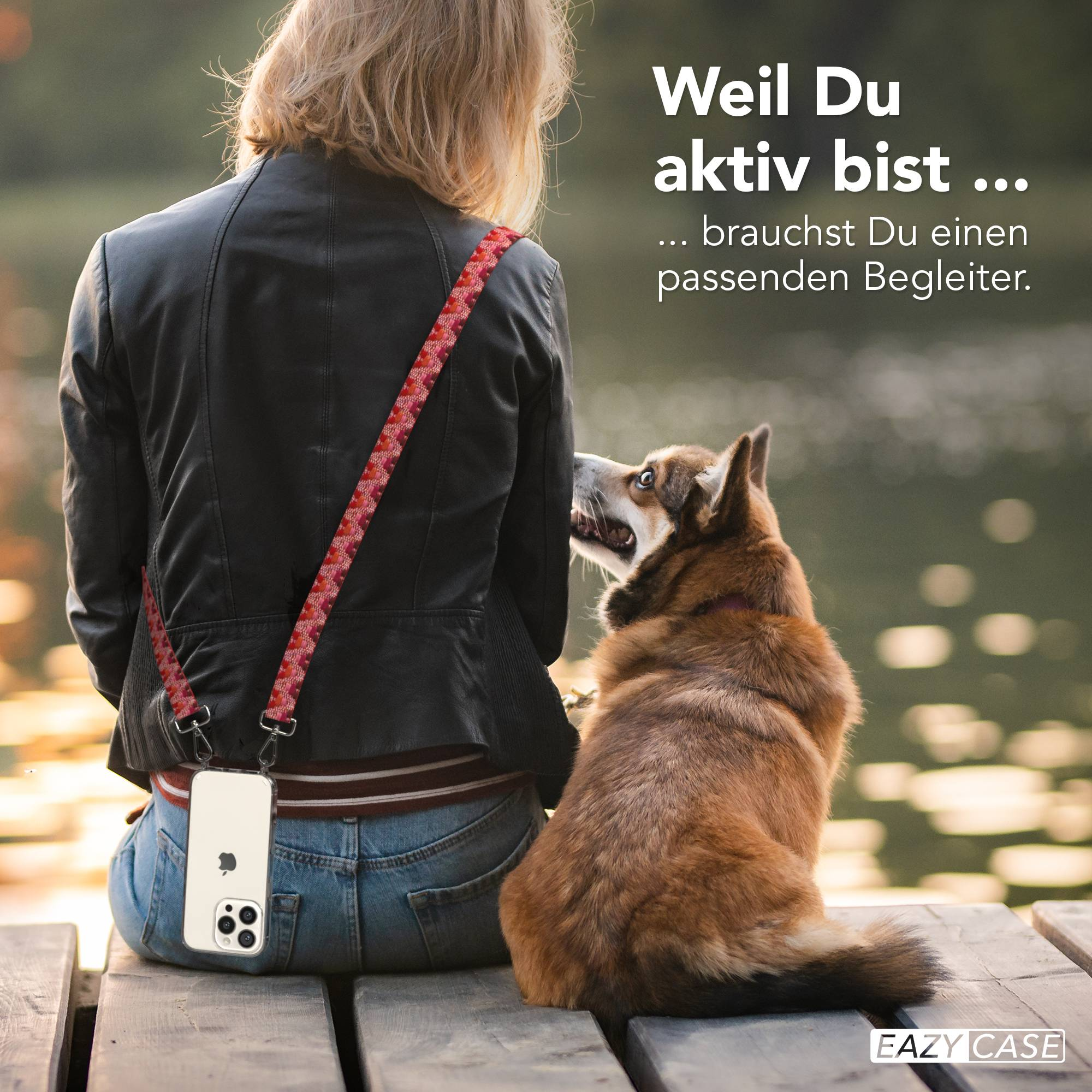 Frau sitzt mit Hund auf Holzsteg. Handy am Trageriemen.