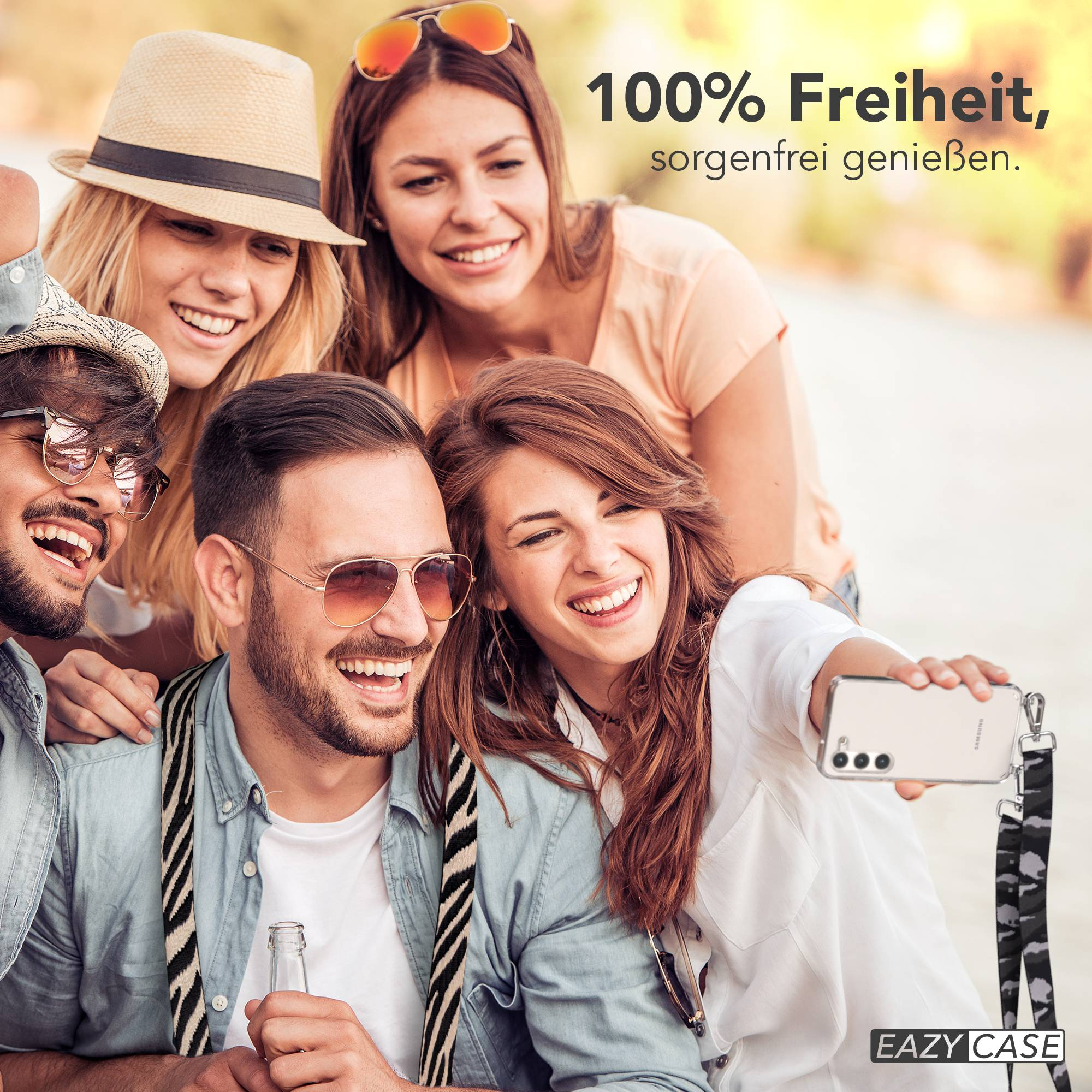 Vier lachende Freunde machen ein Selfie im Freien. Eine Frau hält ein Handy.