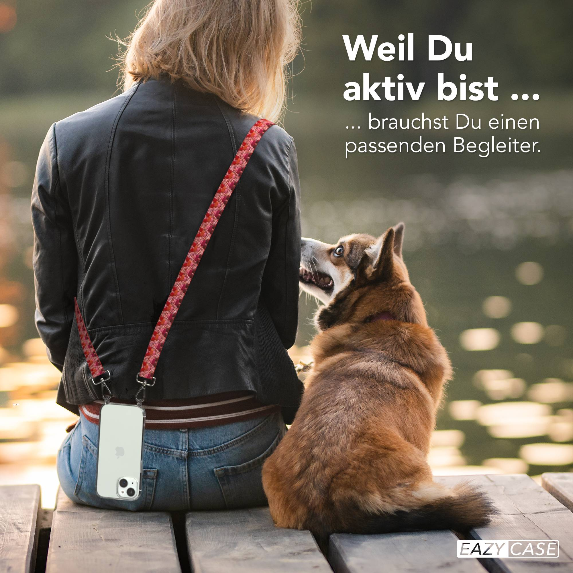Frau in Lederjacke, Jeans und Handy an Tragegurt, mit Hund neben ihr auf einem Holzsteg.