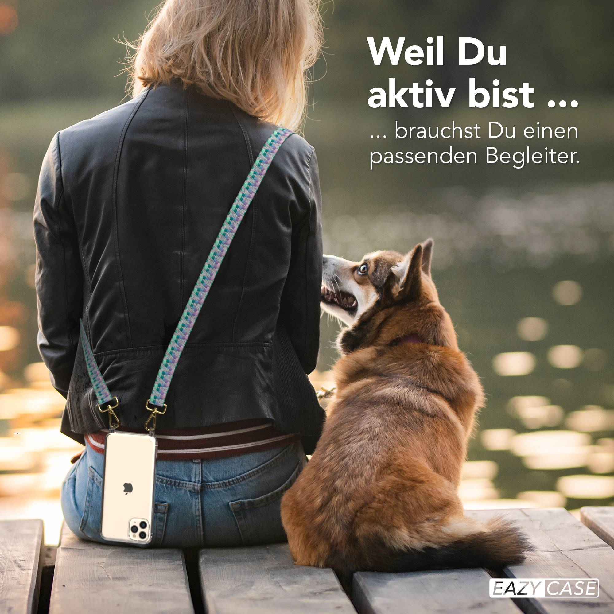 Frau sitzt auf Holzsteg mit Hund, Handy am Gurt, am Wasser.