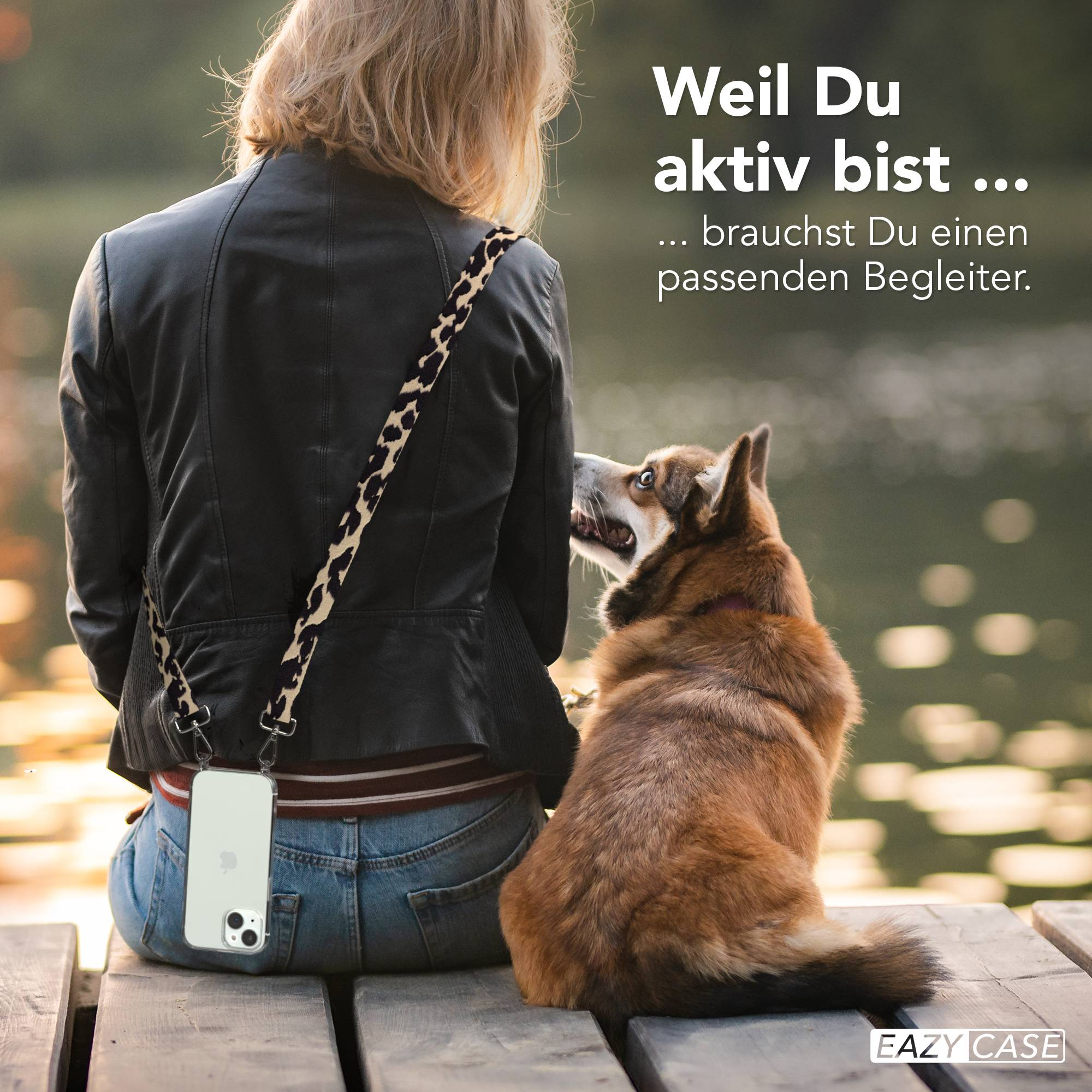 Frau mit Hund sitzt auf Holzplanken am See, Handy mit Leoparden-Gurt.