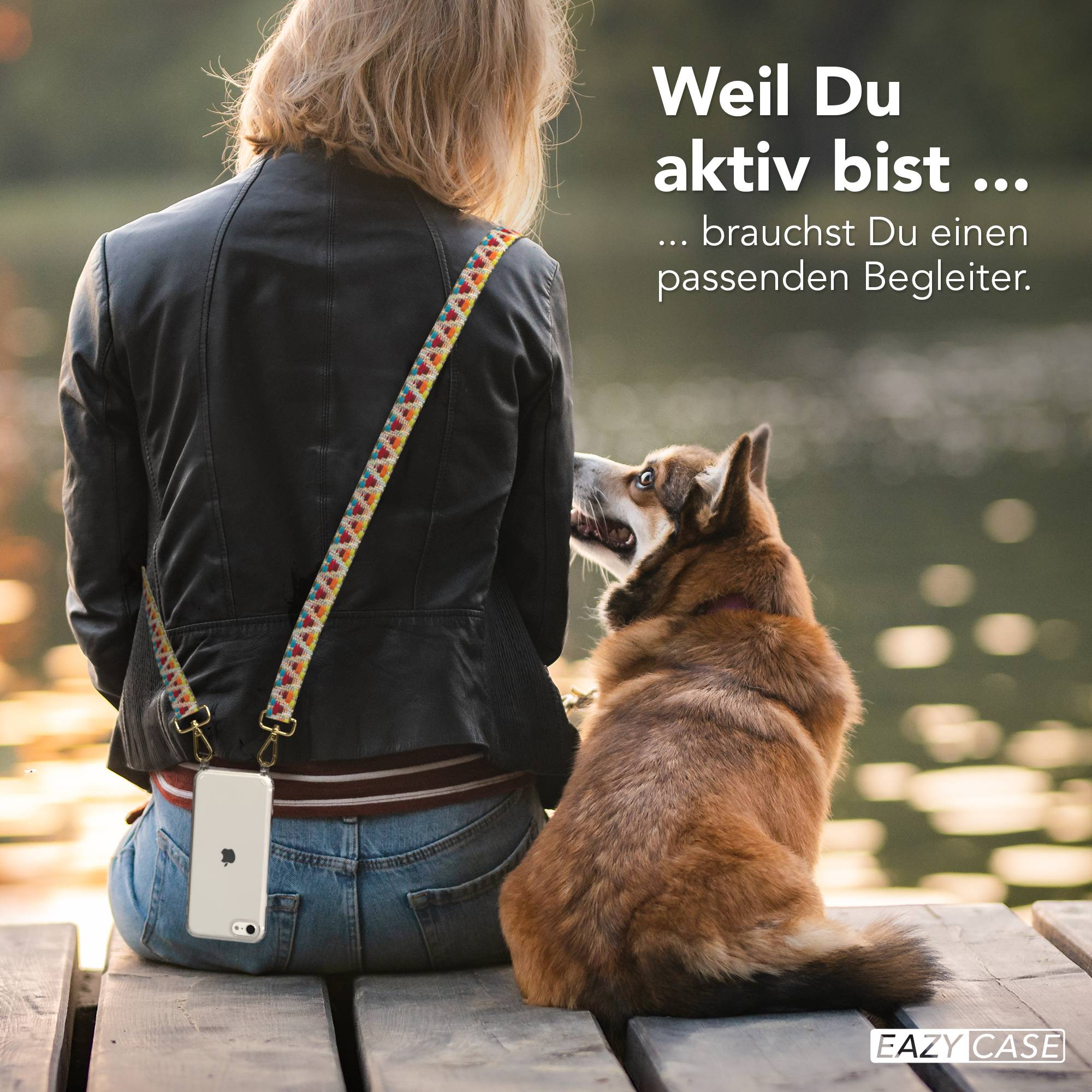 Frau mit Hund sitzt auf Holzsteg. Handy mit Trageriemen. Wasser im Hintergrund.