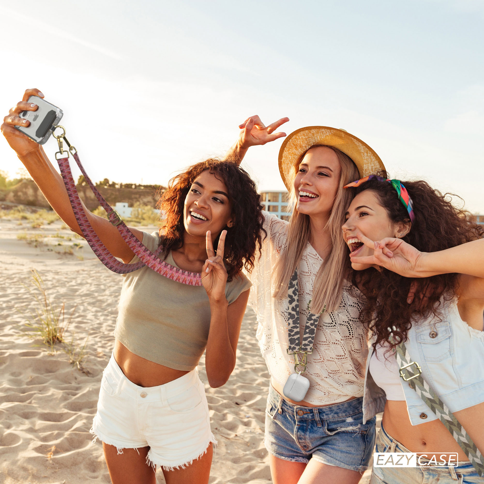 Drei Frauen machen ein Selfie am Strand. Sie tragen Sommerkleidung und haben Spaß.