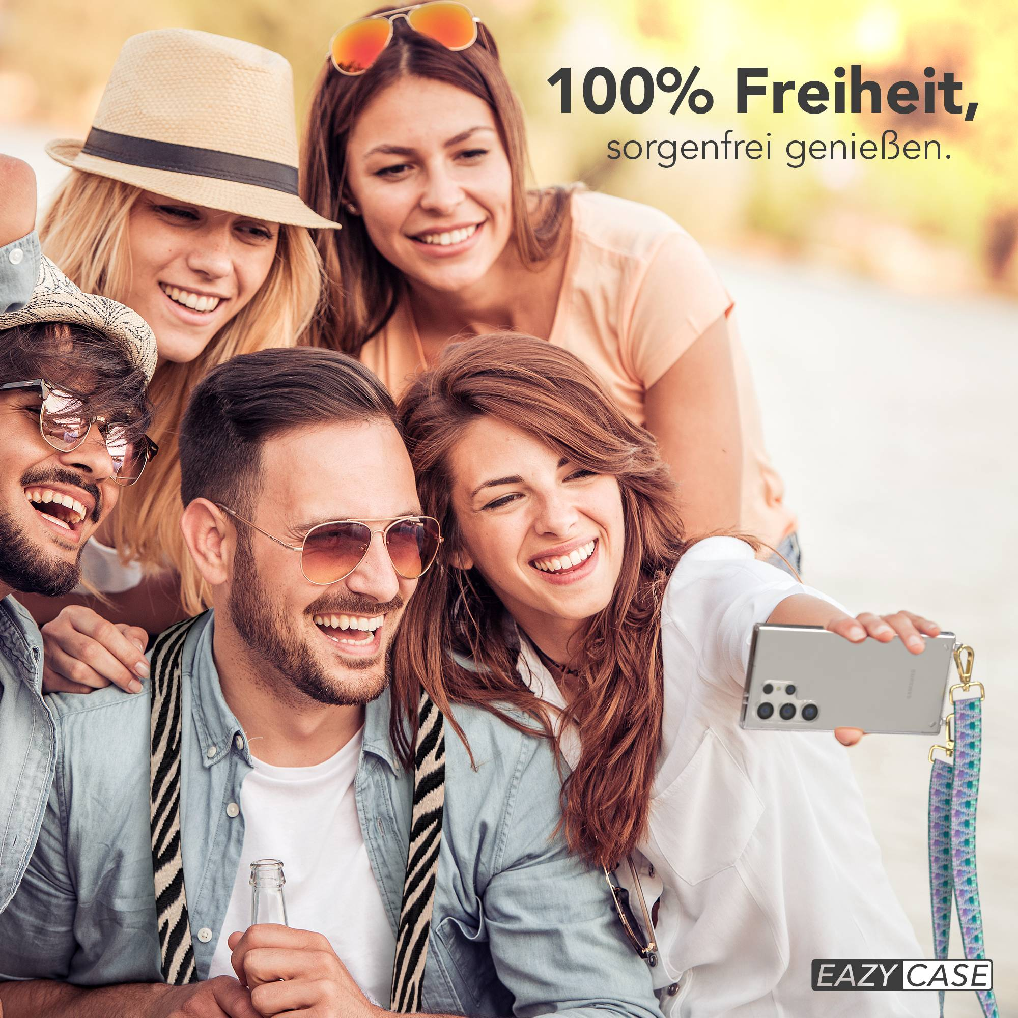 Vier lachende Freunde machen ein Selfie im Freien. Einer hält ein Handy.