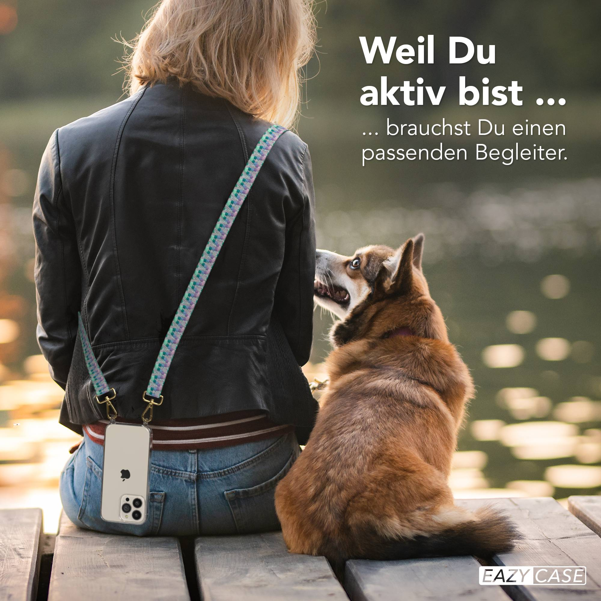 Eine Frau in schwarzer Jacke und Jeans sitzt mit Hund auf Holzsteg. Handy ist am Gurt befestigt.