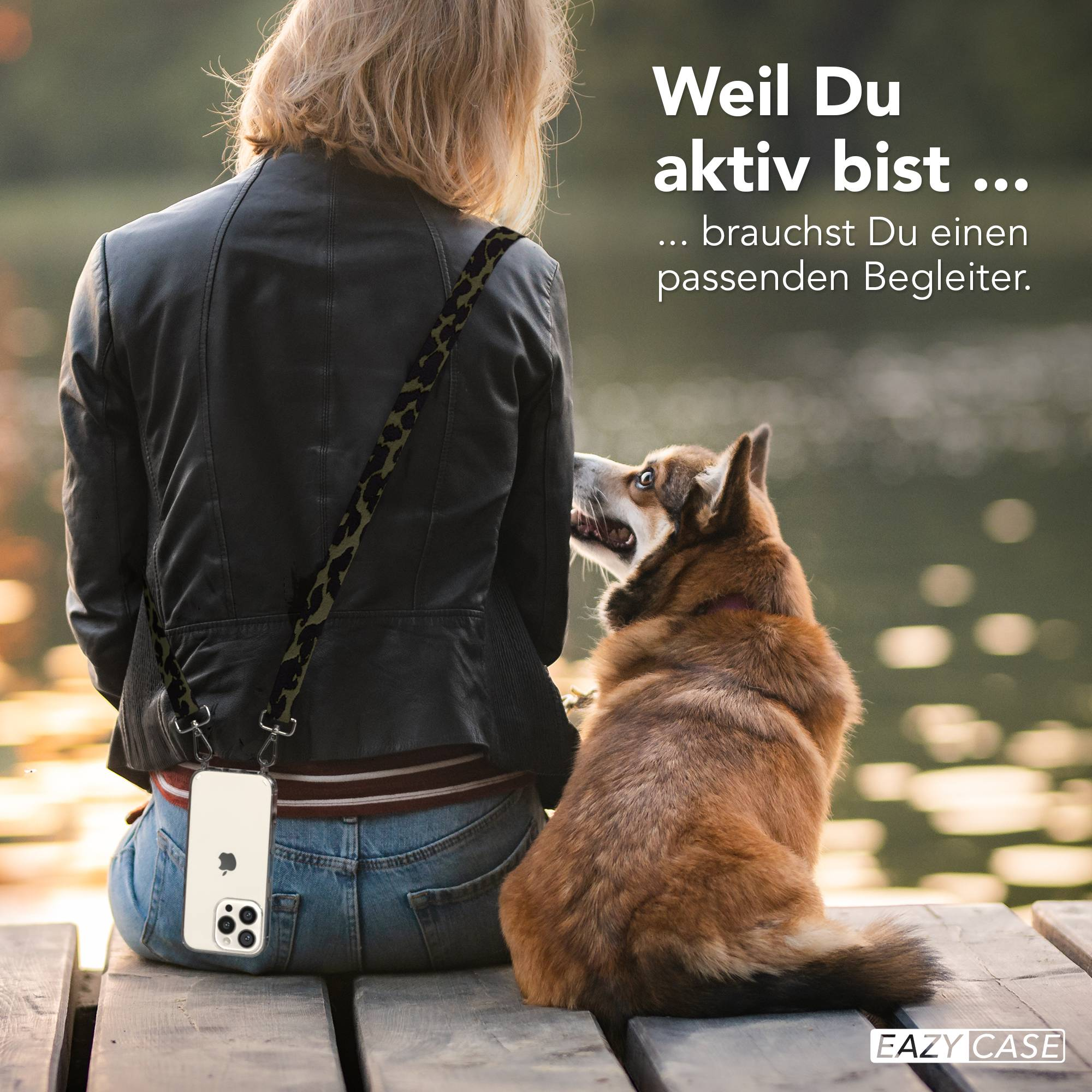 Frau mit Hund sitzt auf Holzsteg am Wasser. Handy hängt am Trageriemen.