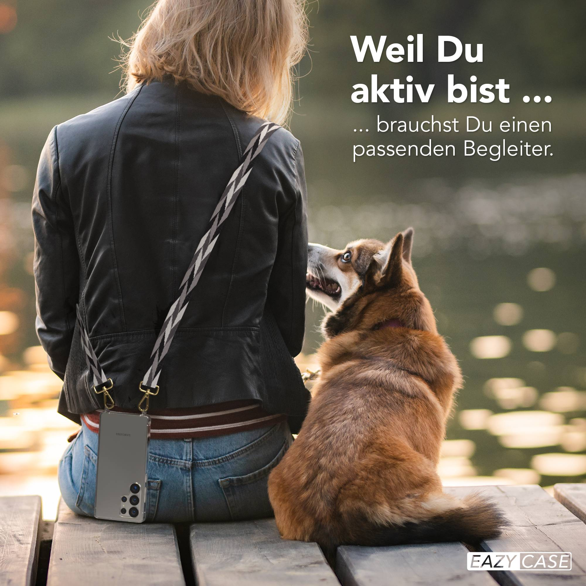 Frau mit Hund sitzt auf Holzsteg am Wasser. Handy am Träger.