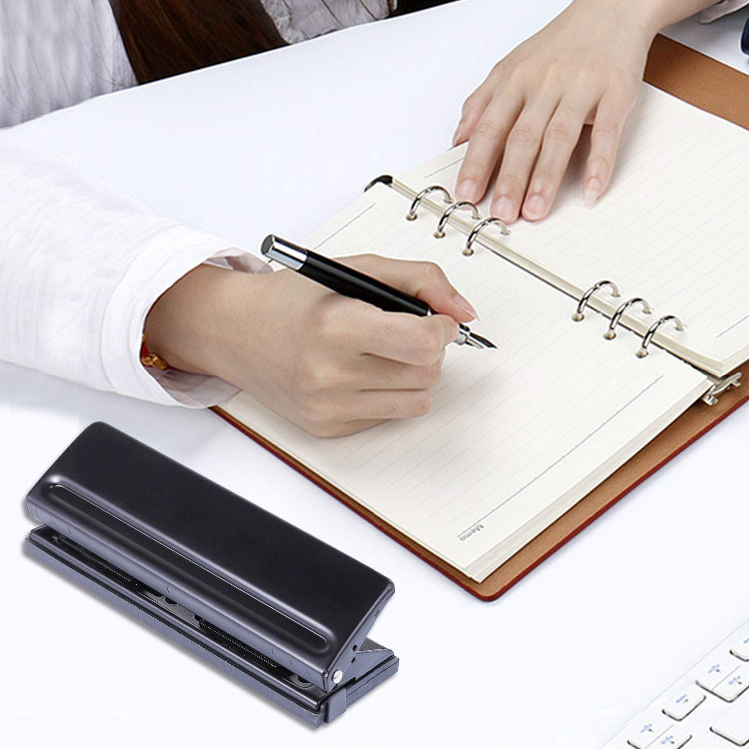 Hände schreiben in ein Notizbuch mit Stift, schwarzer Locher auf Schreibtisch.