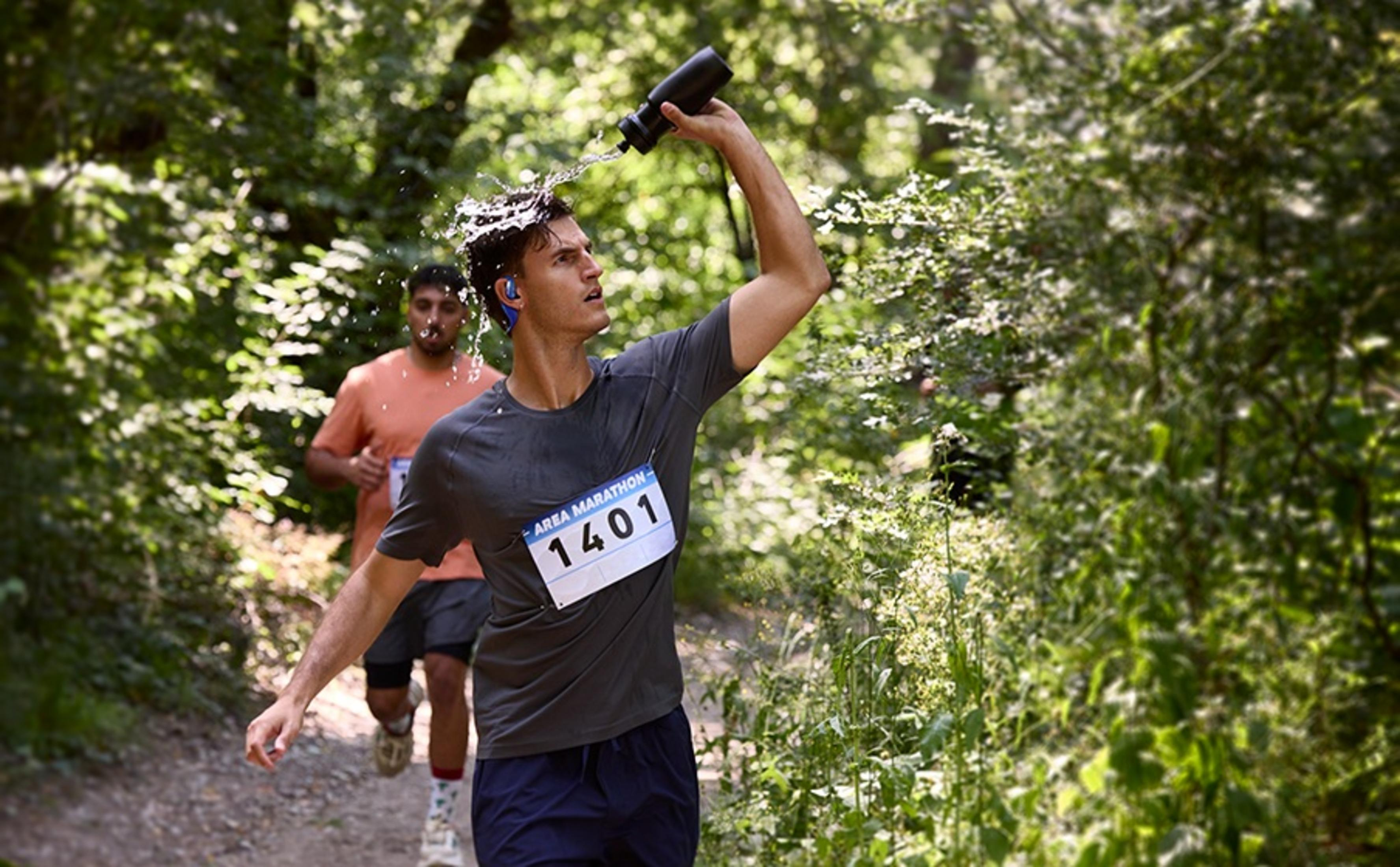 Biegacz polewa głowę wodą podczas maratonu. Drugi biegacz podąża.