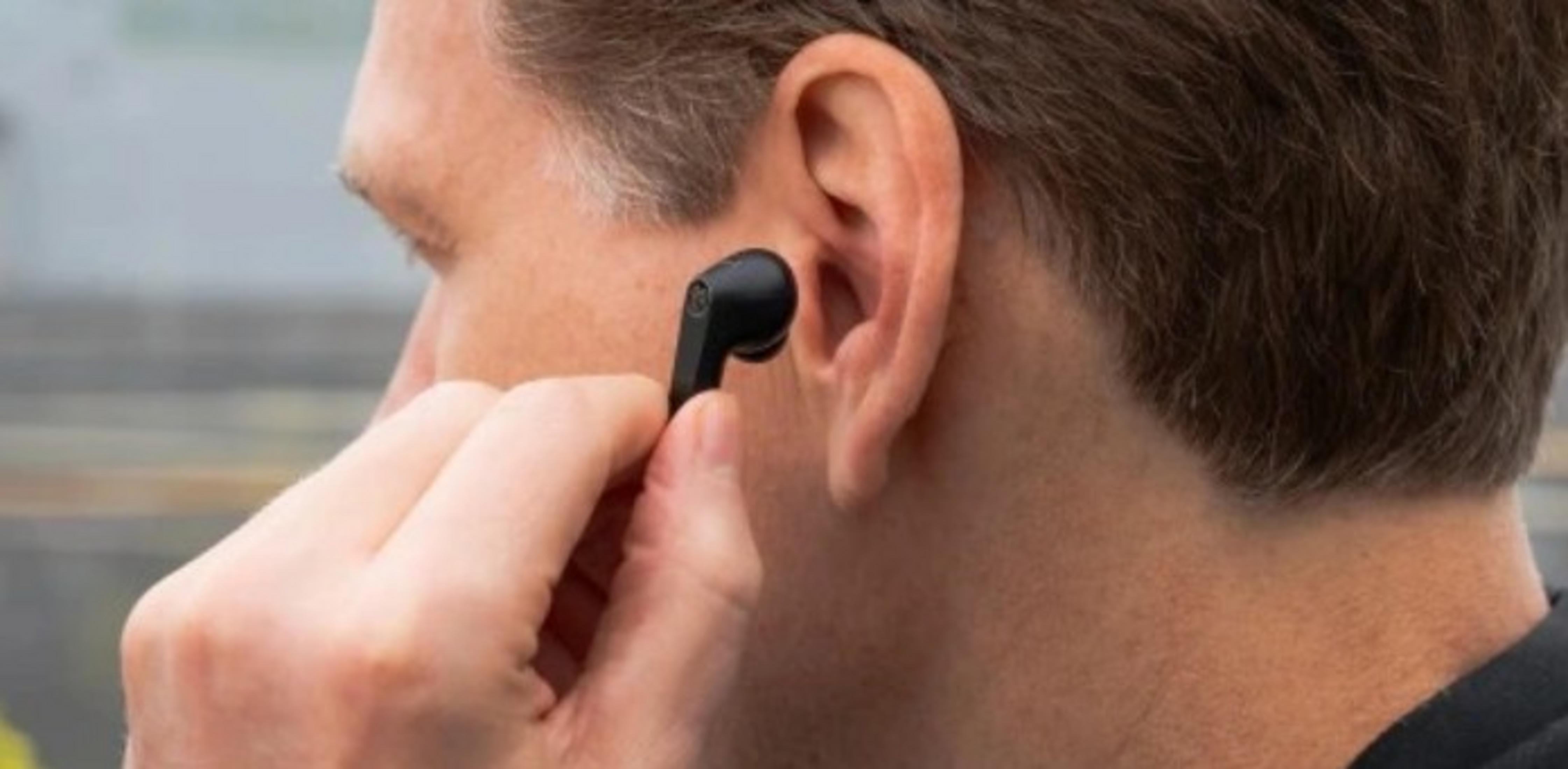 Una persona inserisce un auricolare wireless nero nell'orecchio. Primo piano.