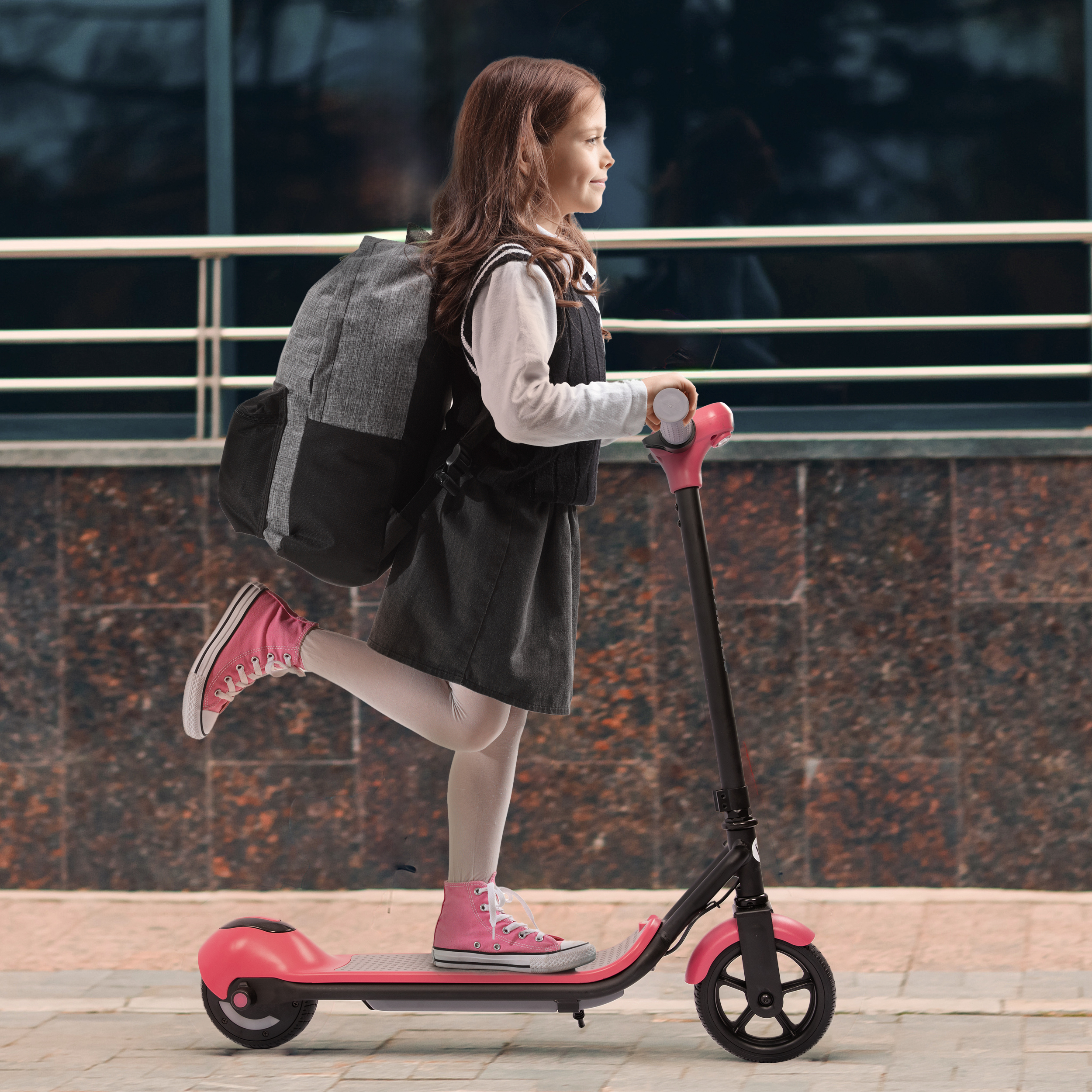Ein Mädchen mit Rucksack fährt auf einem pinken Roller.