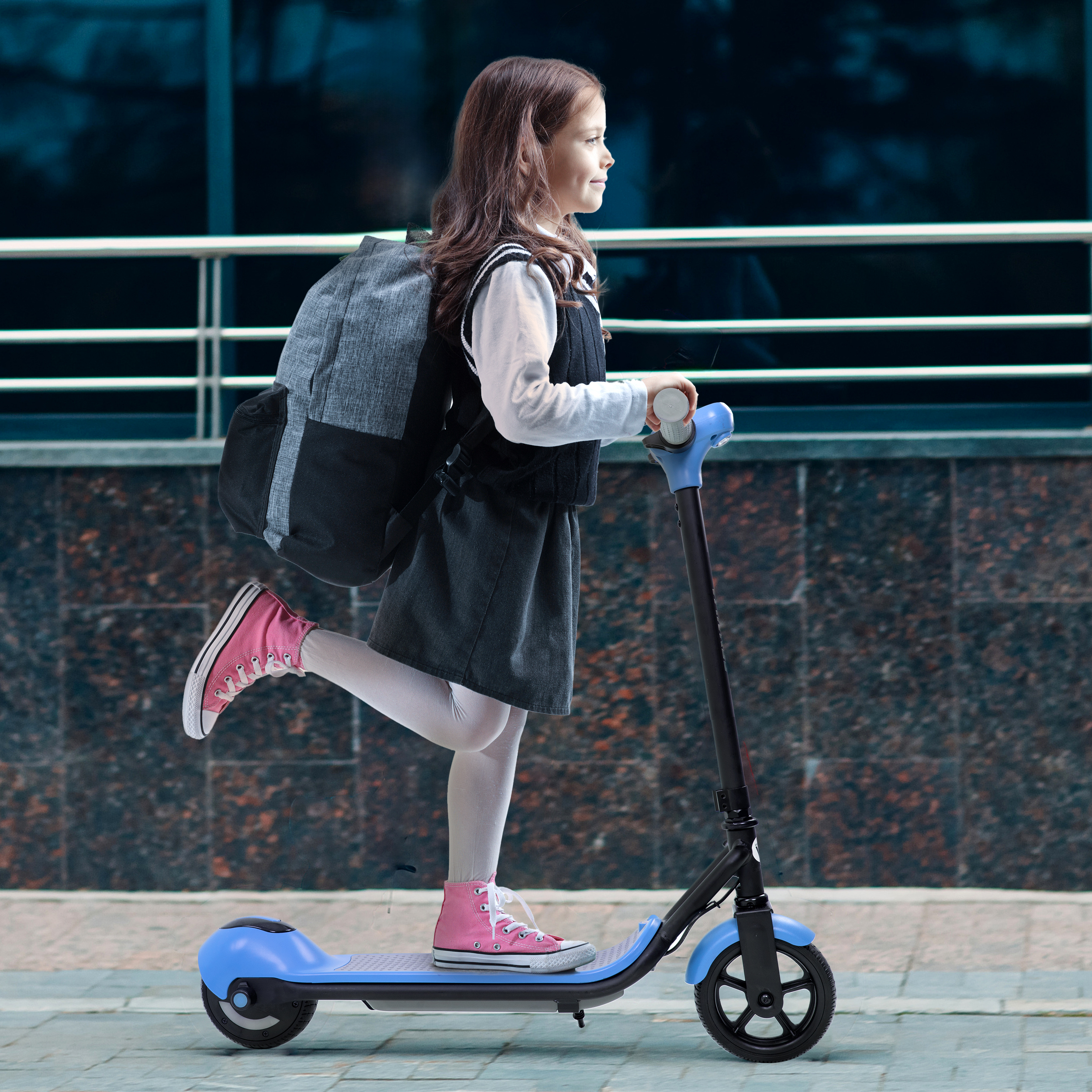 Ein Mädchen in Schuluniform fährt einen blauen Elektroroller mit Rucksack.