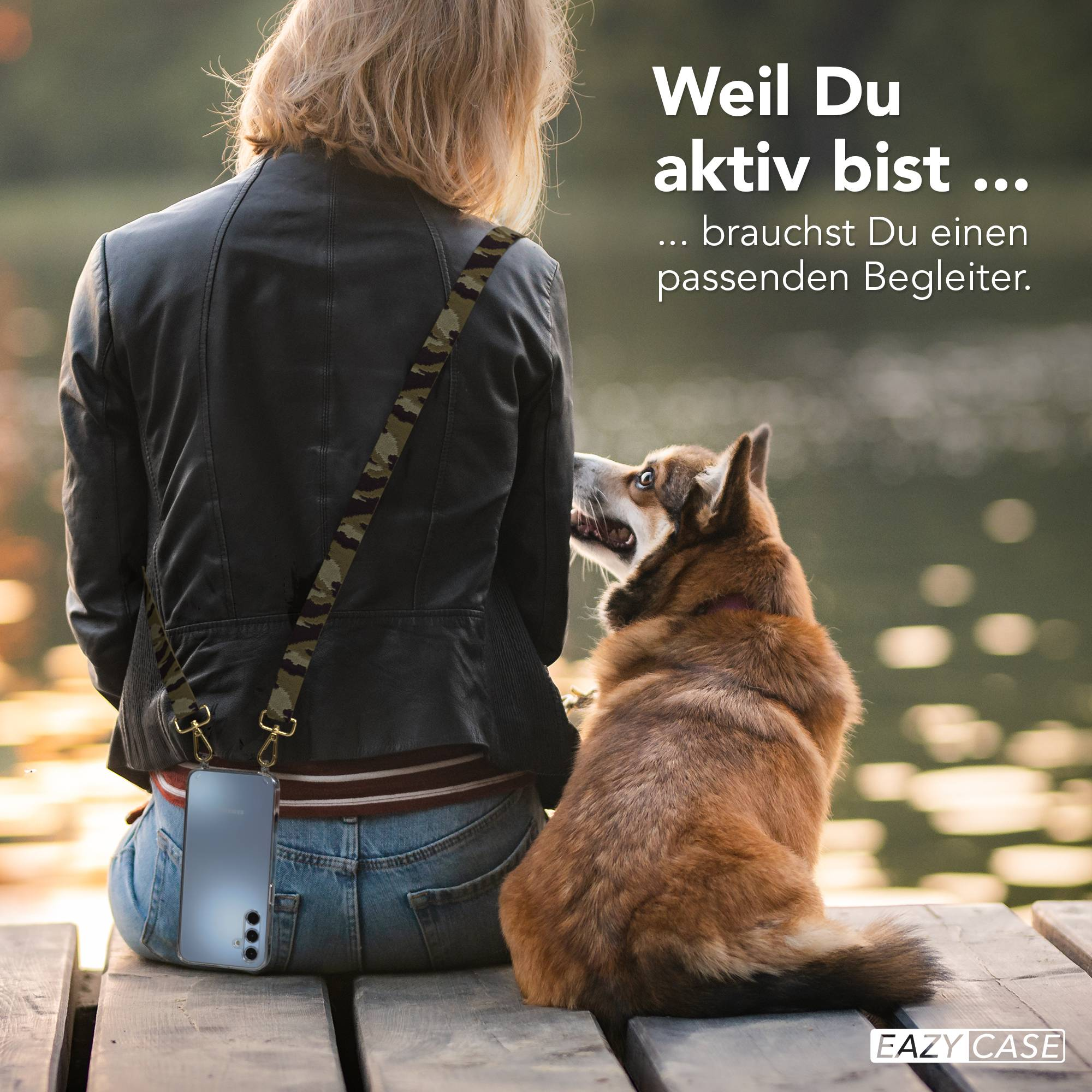 Frau mit Hund sitzt auf Holzsteg, Handy hängt an Camo-Gurt. Wasser im Hintergrund.