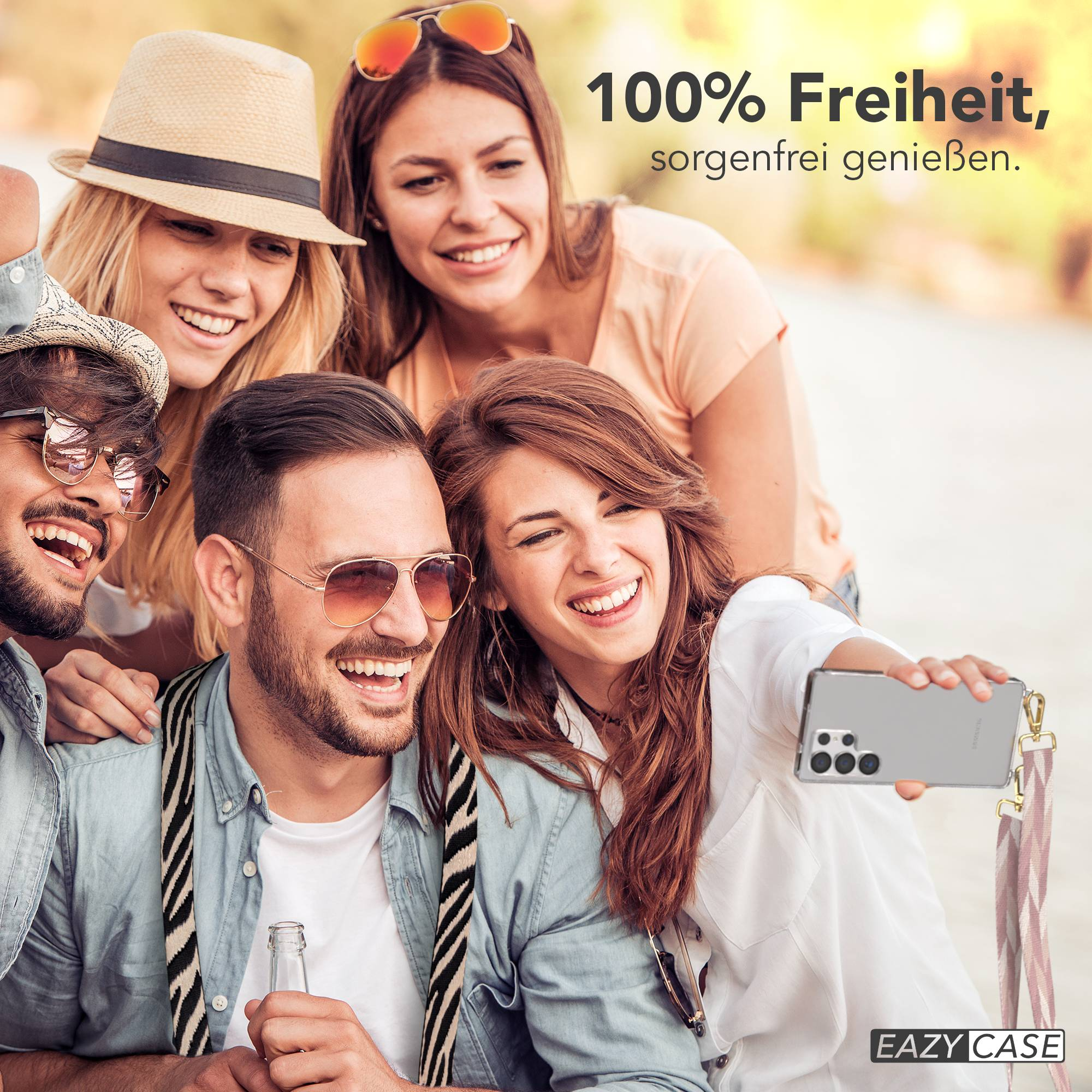 Vier Freunde lächeln und machen draußen ein Selfie. Eine Frau hält ein Handy.