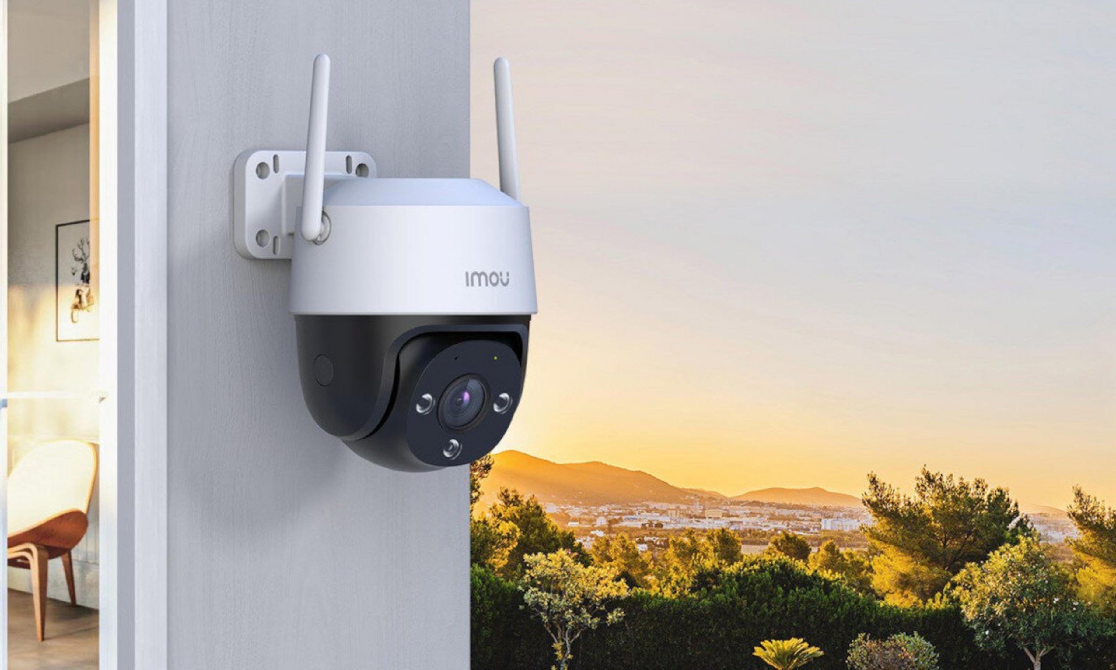 Telecamera di sicurezza bianca montata su muro, con vista su città e colline al tramonto.