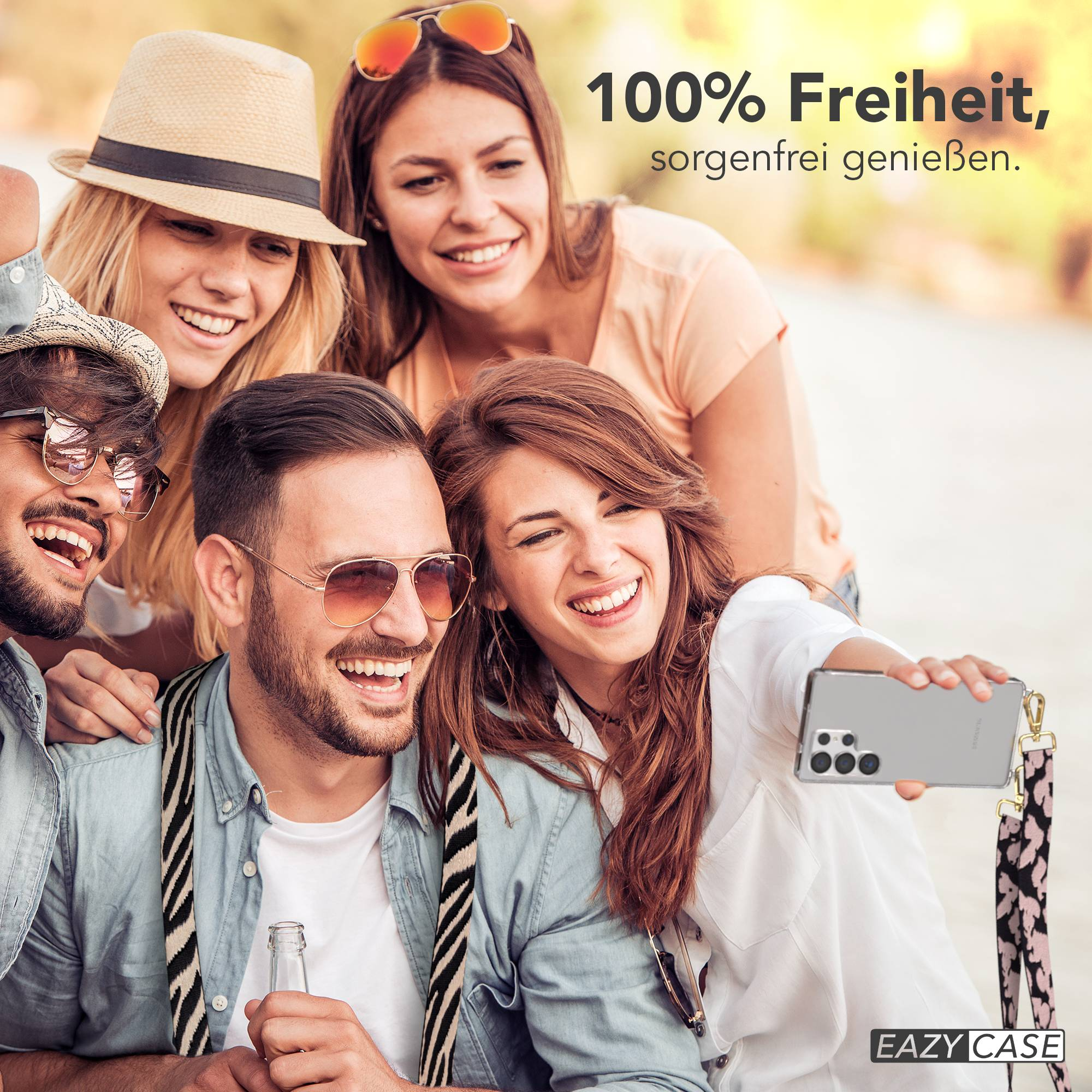 Vier lachende Freunde machen ein Selfie im Freien, eine Frau hält ein Handy.