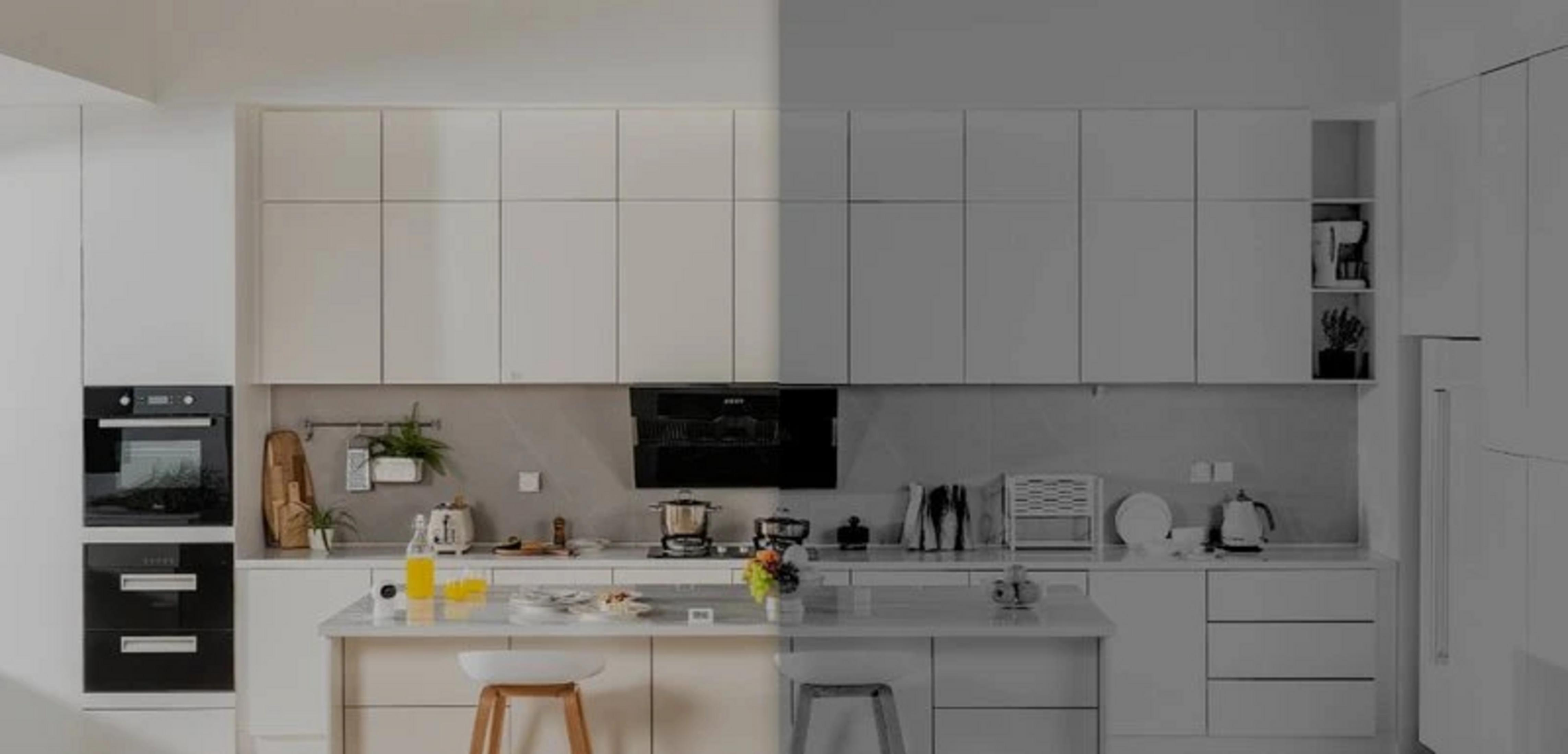 Nowoczesna kuchnia z białymi szafkami, piekarnikami, wyspą i płytą grzewczą. Niektóre obszary kolorowe, inne w skali szarości.