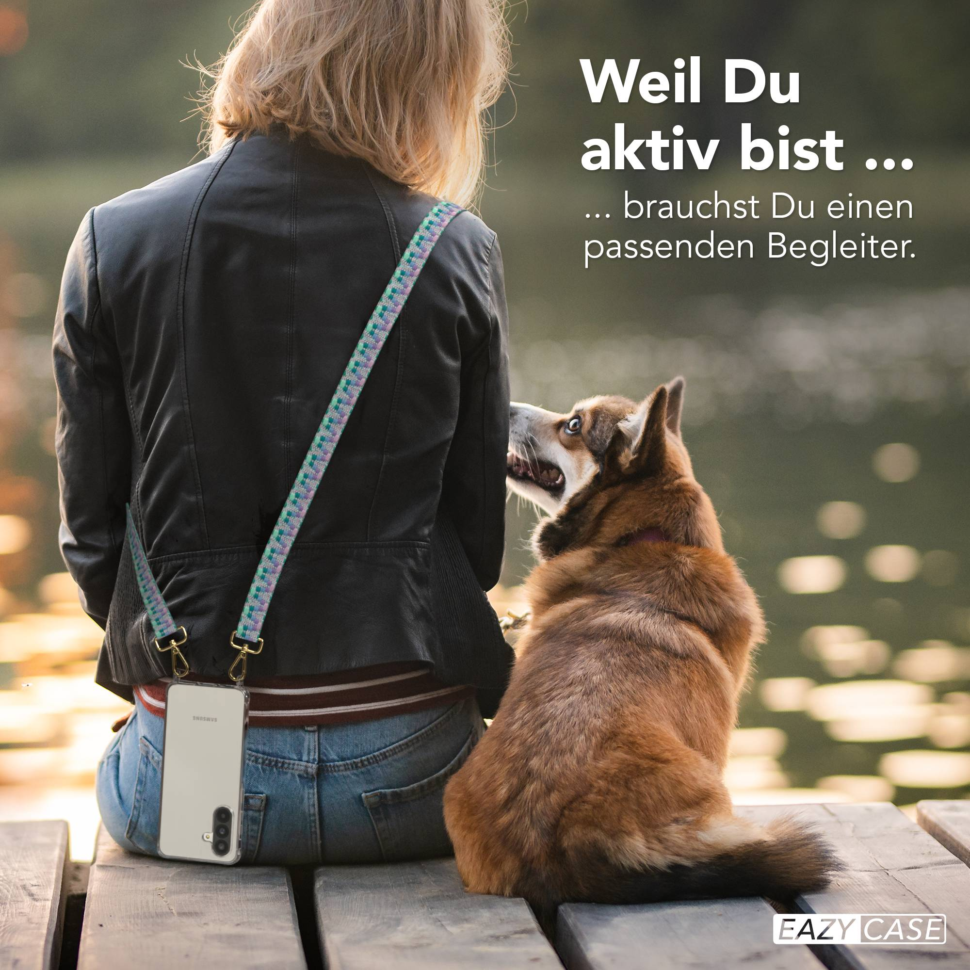 Eine Person sitzt mit einem Hund auf einem Steg, ein Handy hängt an einem Riemen über der Schulter.