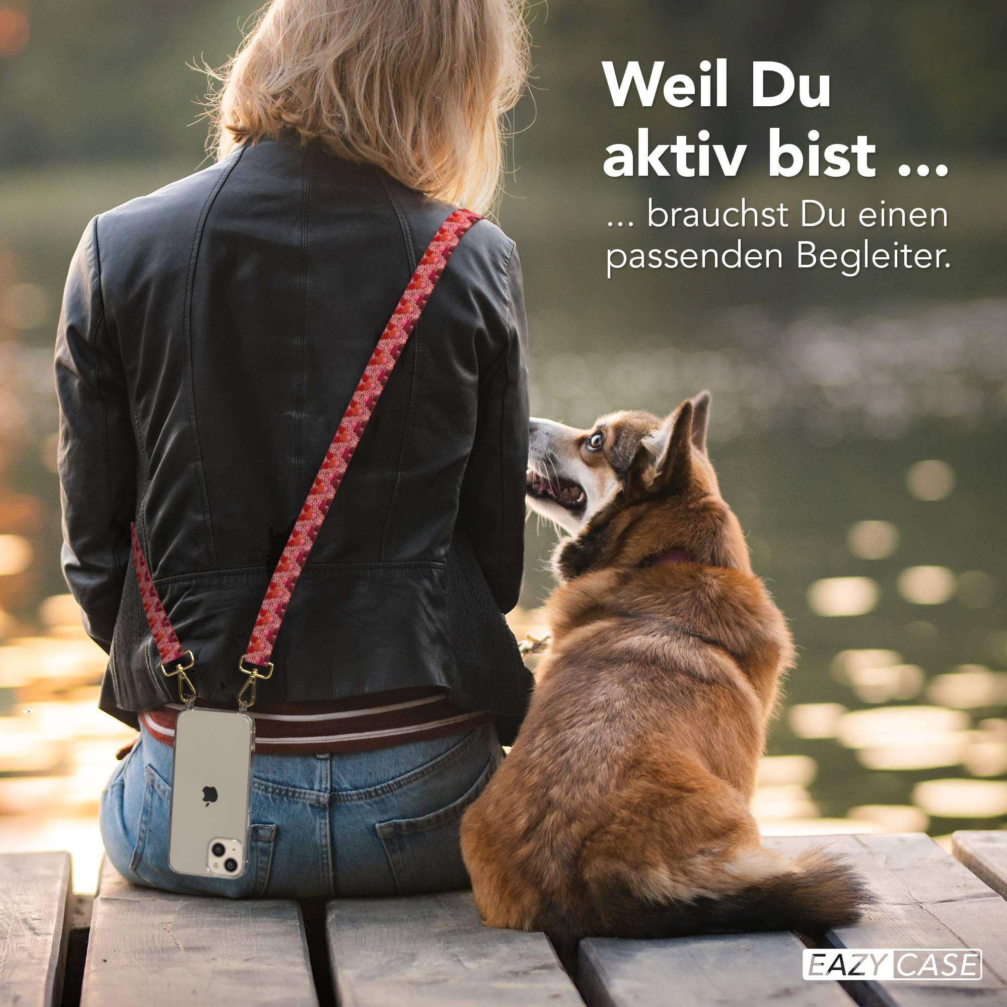 Frau mit Hund sitzt auf einer Holzplanke am Wasser, Handy am Trageriemen.