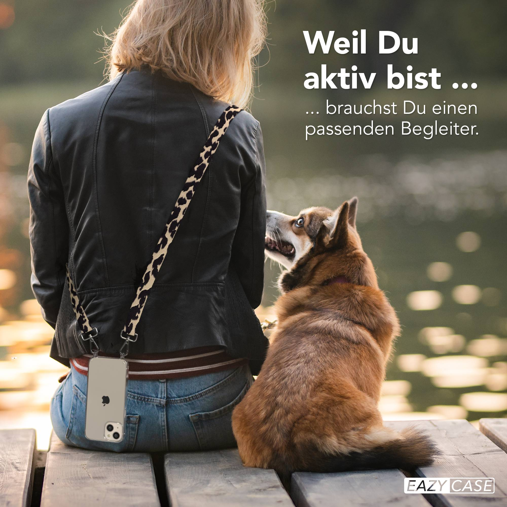 Frau mit Hund sitzt auf einer Holzbank am Wasser, mit Handy-Tasche.