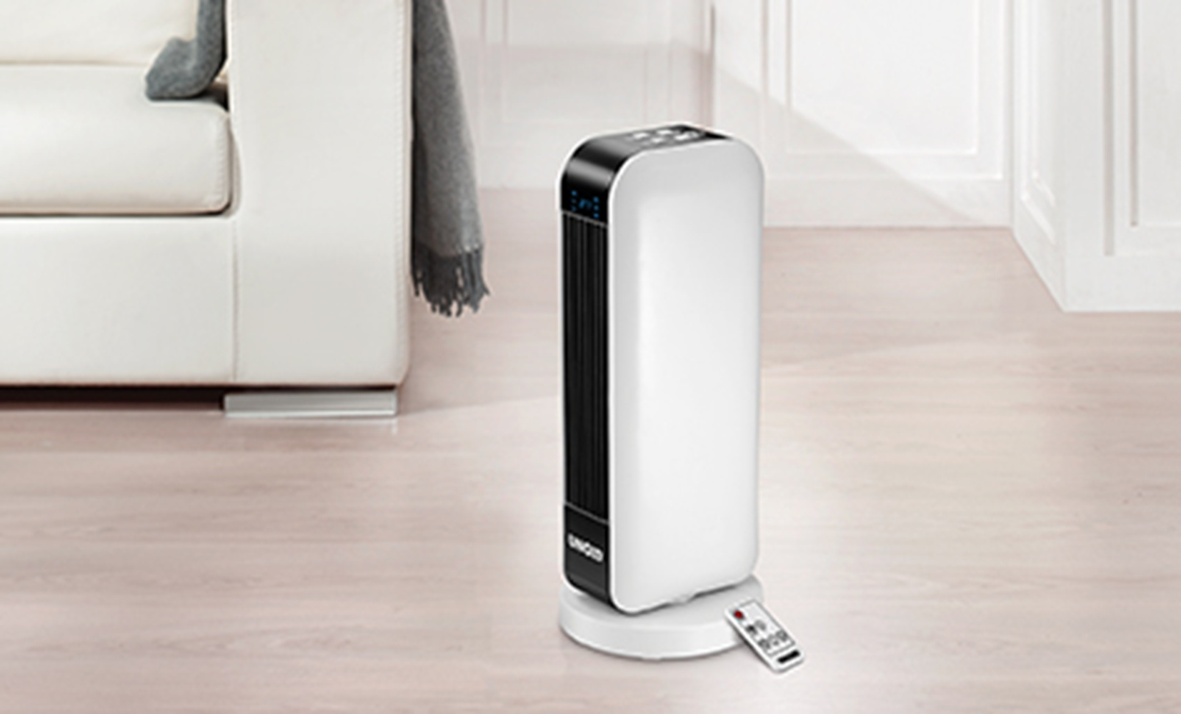 Biały i czarny grzejnik wieżowy z pilotem na jasnej drewnianej podłodze obok kanapy.