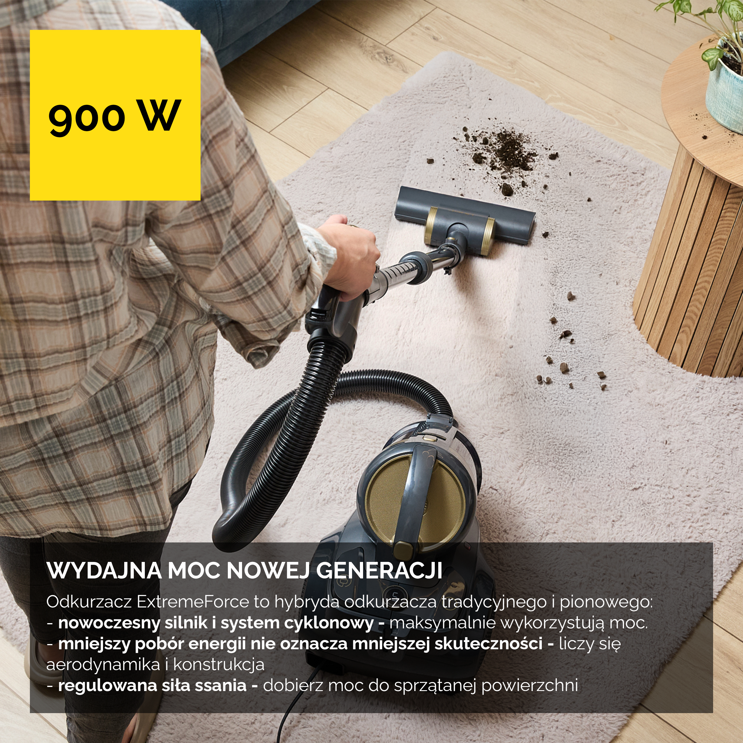Osoba odkurza dywan szarym odkurzaczem. Żółte pudełko 900 W.