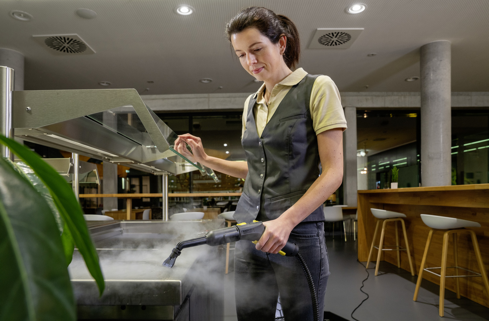 Kobieta czyści powierzchnię parownicą w nowoczesnym budynku.